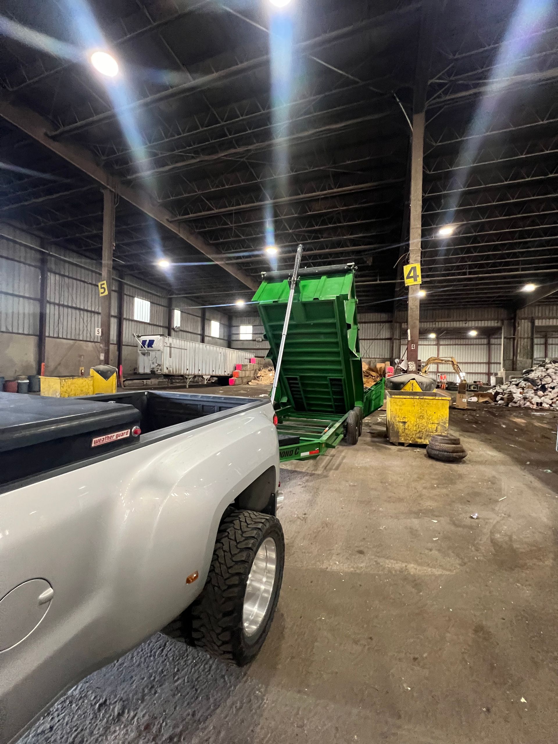 A white truck is parked in a warehouse next to a green dumpster.