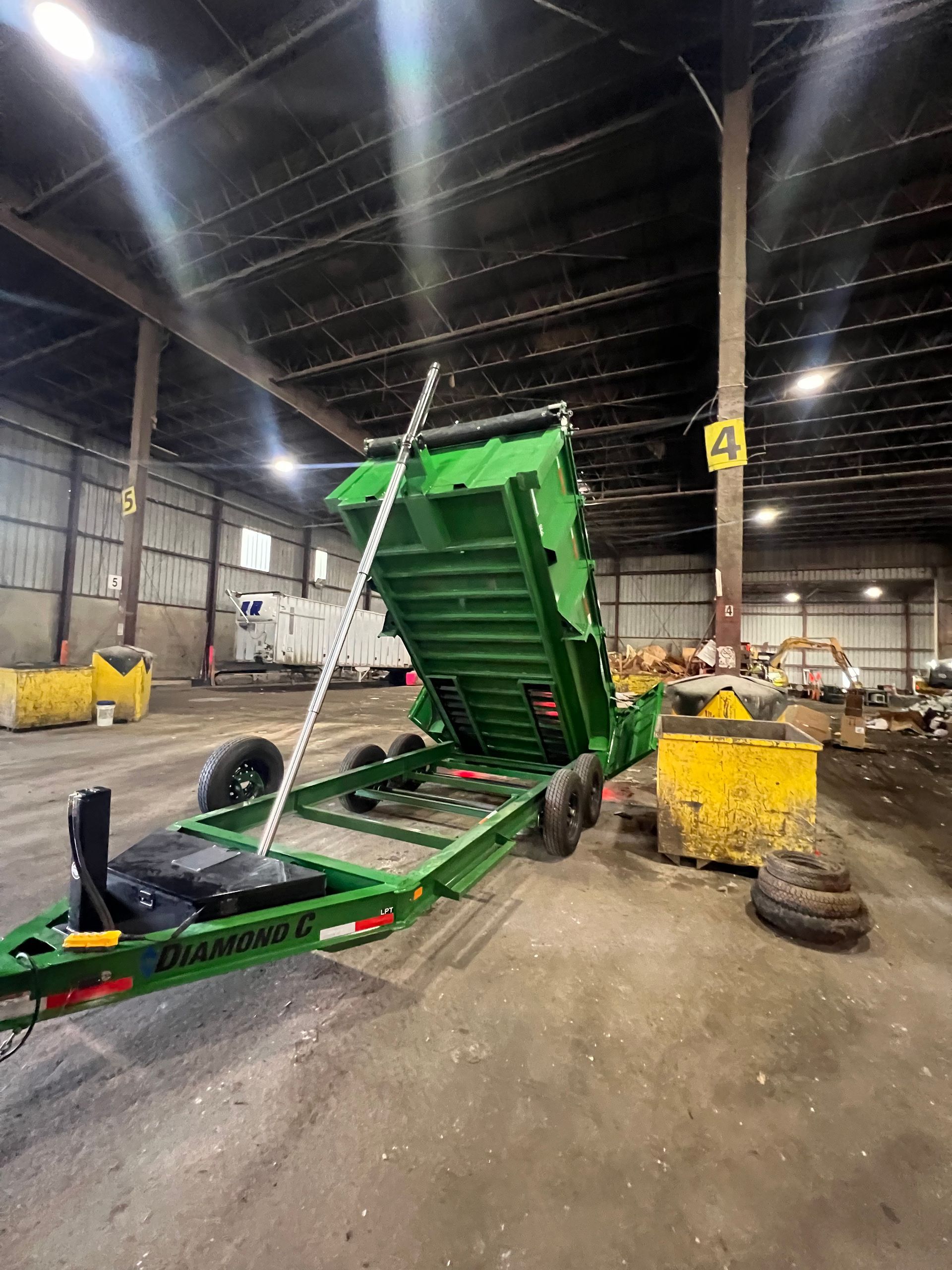 A green dump trailer is parked in a warehouse.