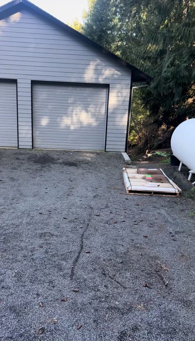 A garage with two garage doors and a propane tank in front of it.