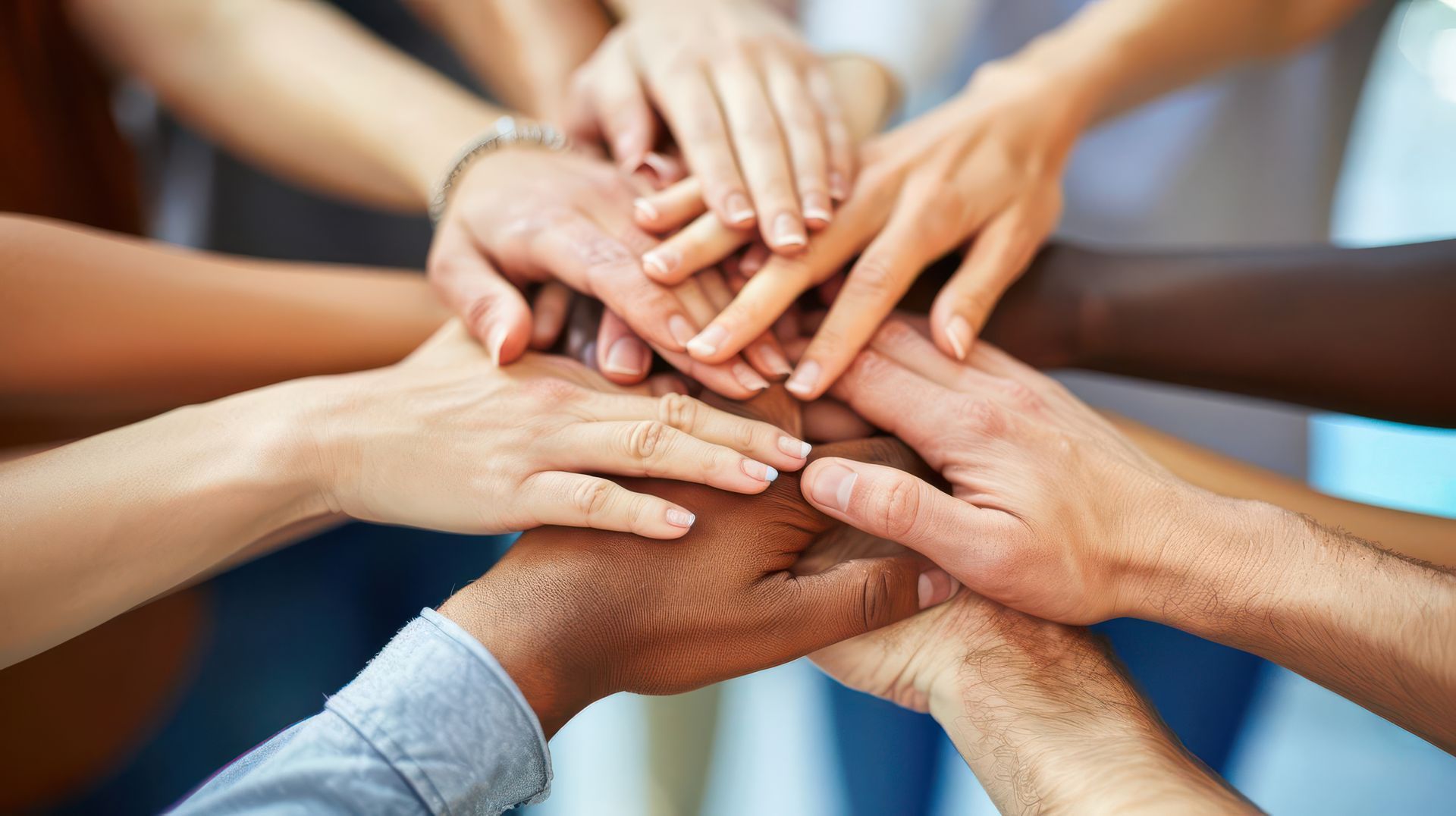 Hands of various skin tones clasped together in a pile, symbolizing unity and teamwork.