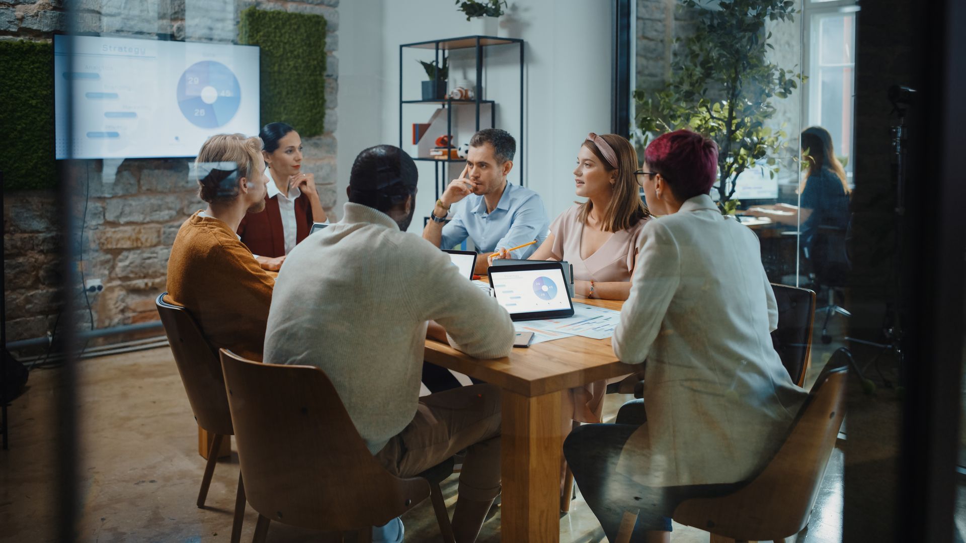 People at a table in a modern office, discussing charts and graphs, some are looking at the screen.