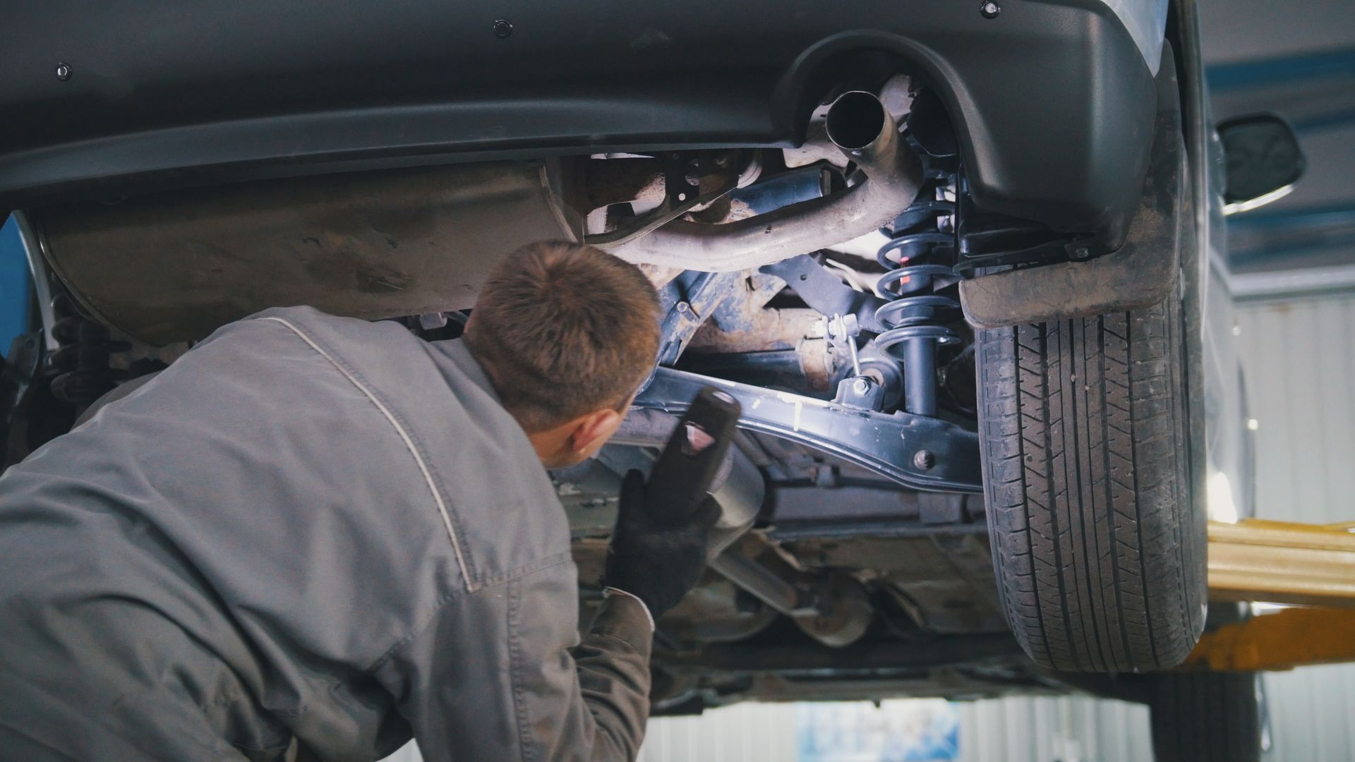 A mechanic is working on the underside of a car