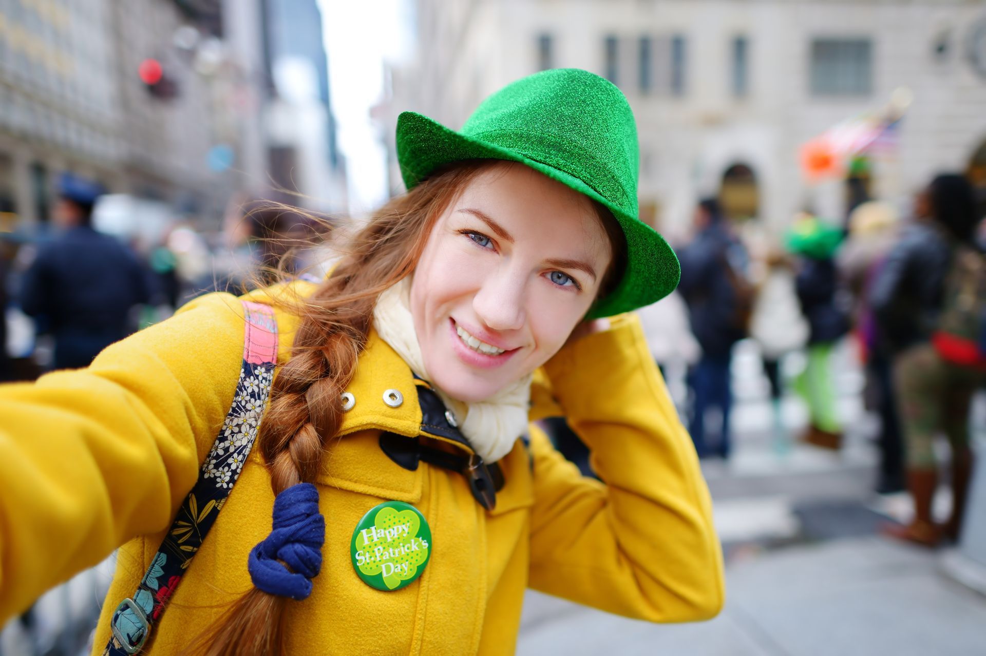 Woman in green hat and yellow coat takes a selfie in a crowd on St. Patrick's Day.