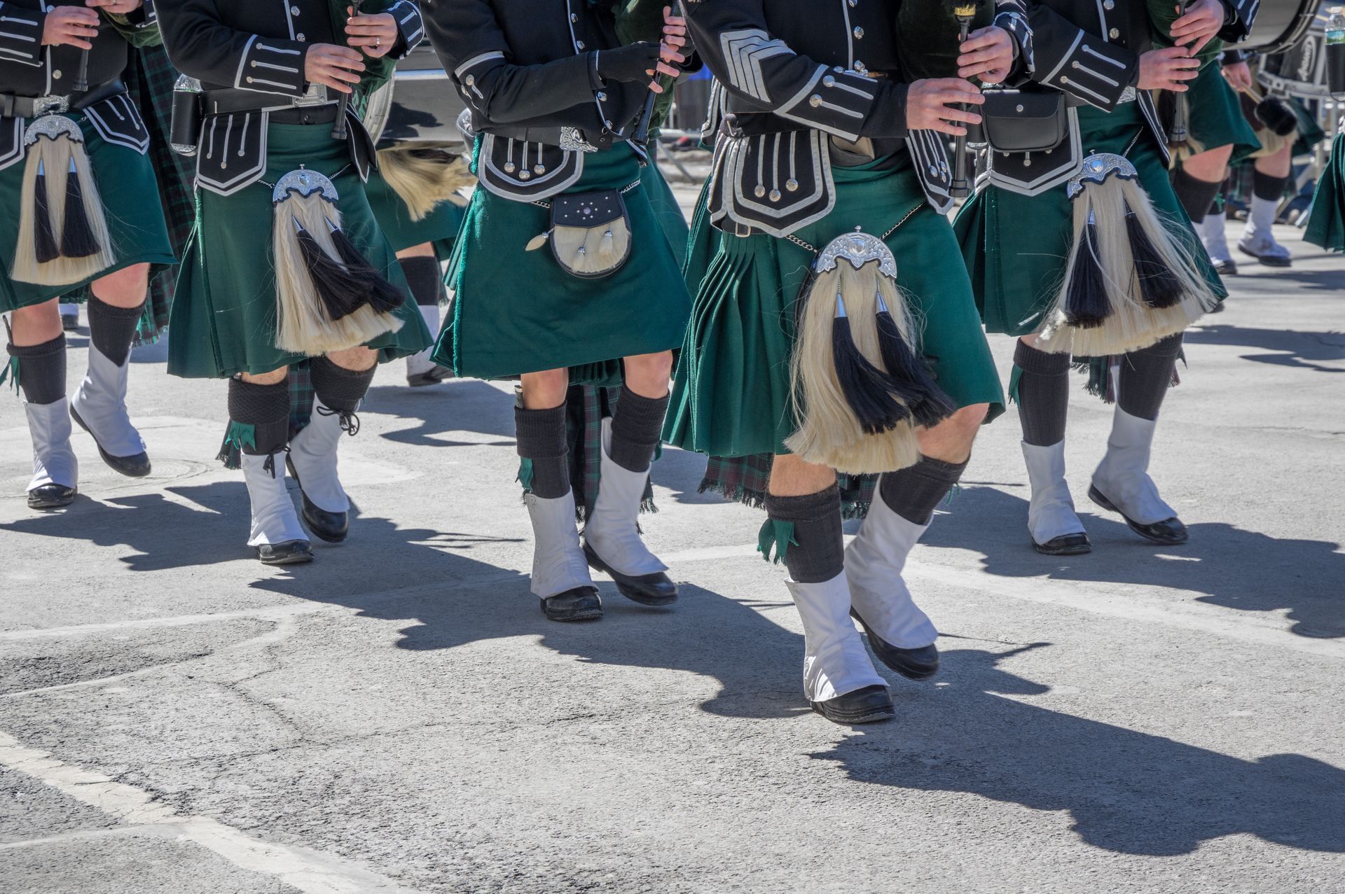 A group of people in kilts are marching down a street.