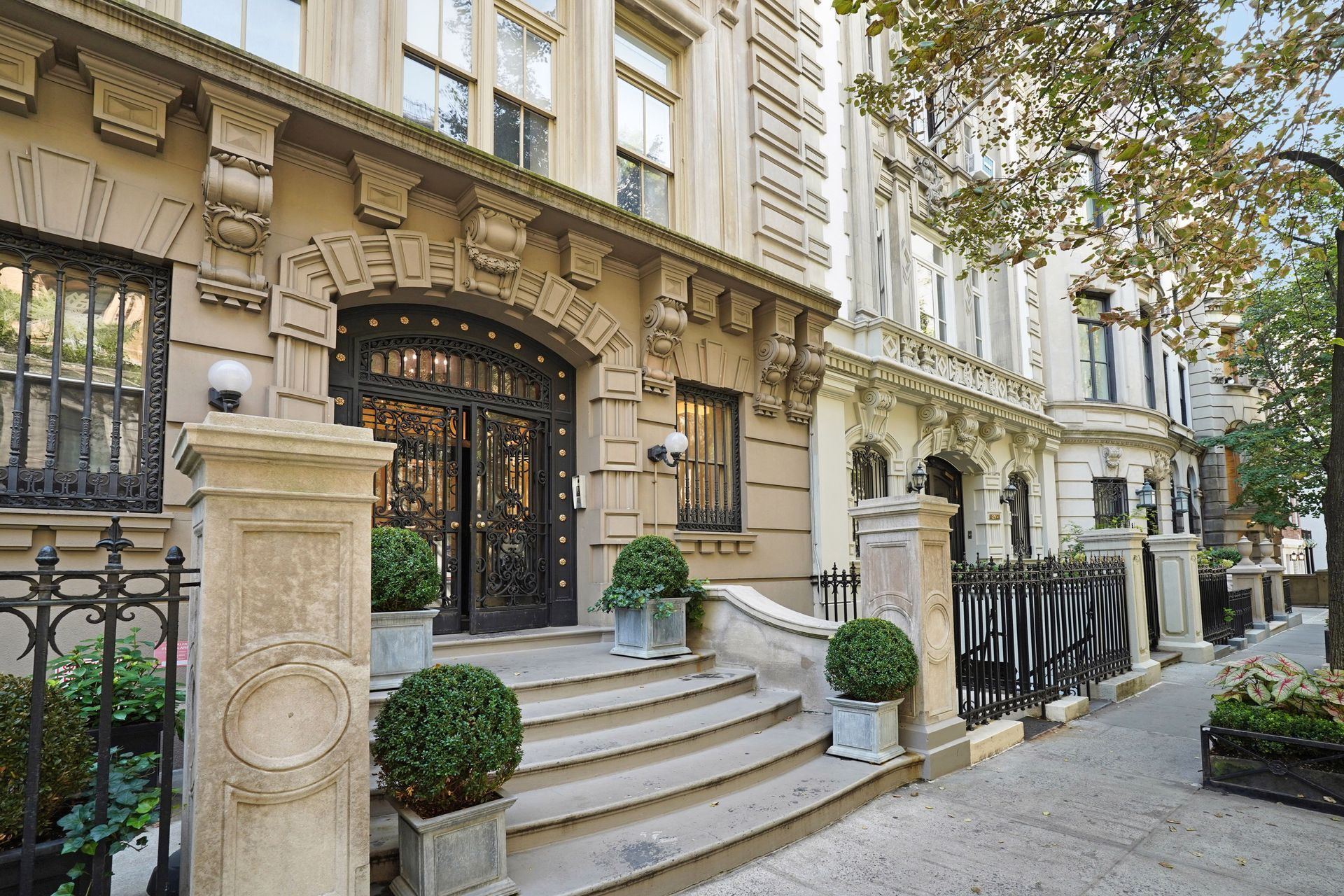 Stone townhouses with ornate entryways and wrought-iron details, lined up on a city sidewalk.