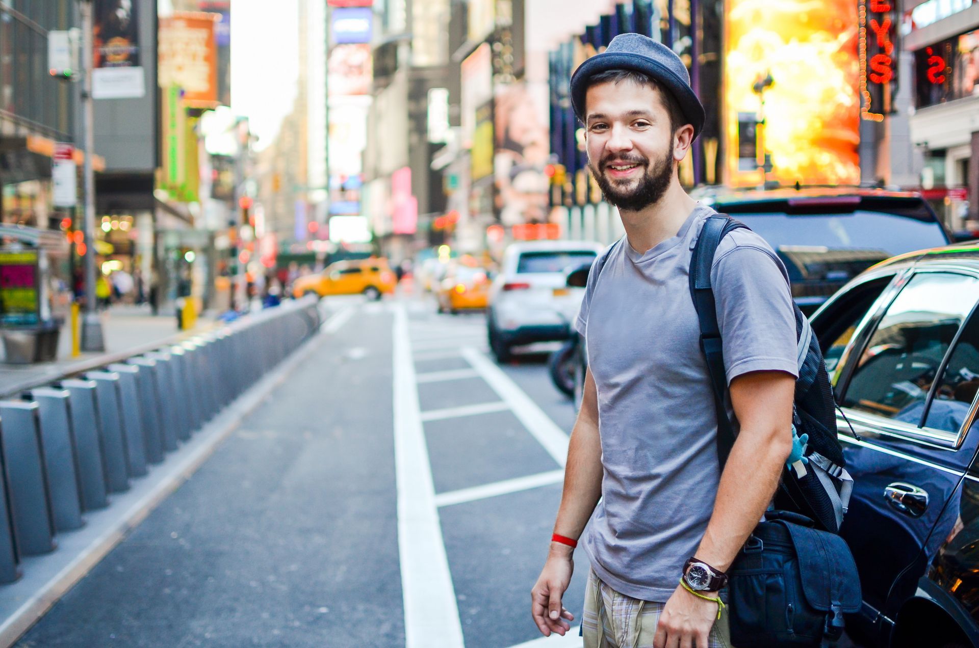 Man with backpack smiles at camera in Times Square, NYC.