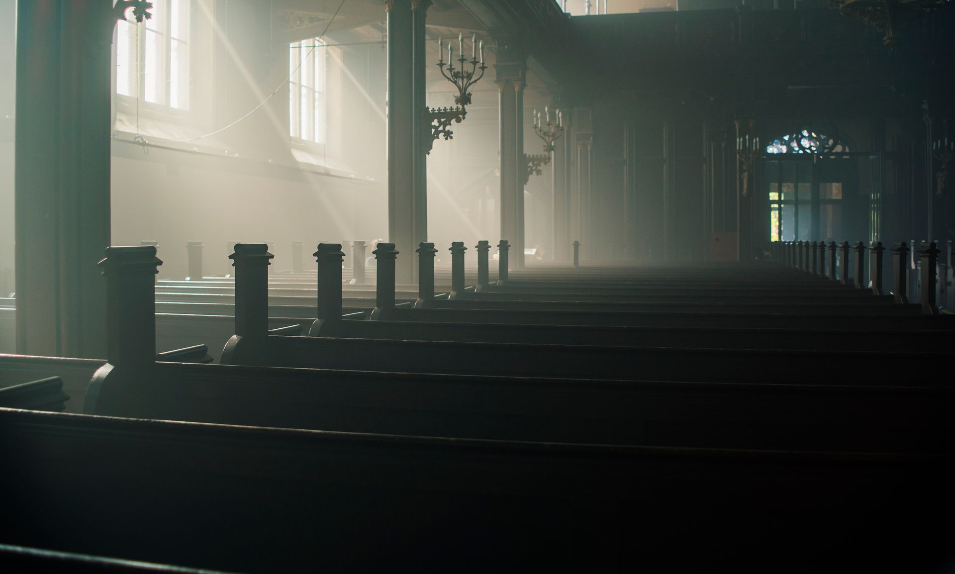 Sunlight streams through windows, illuminating rows of empty church pews.