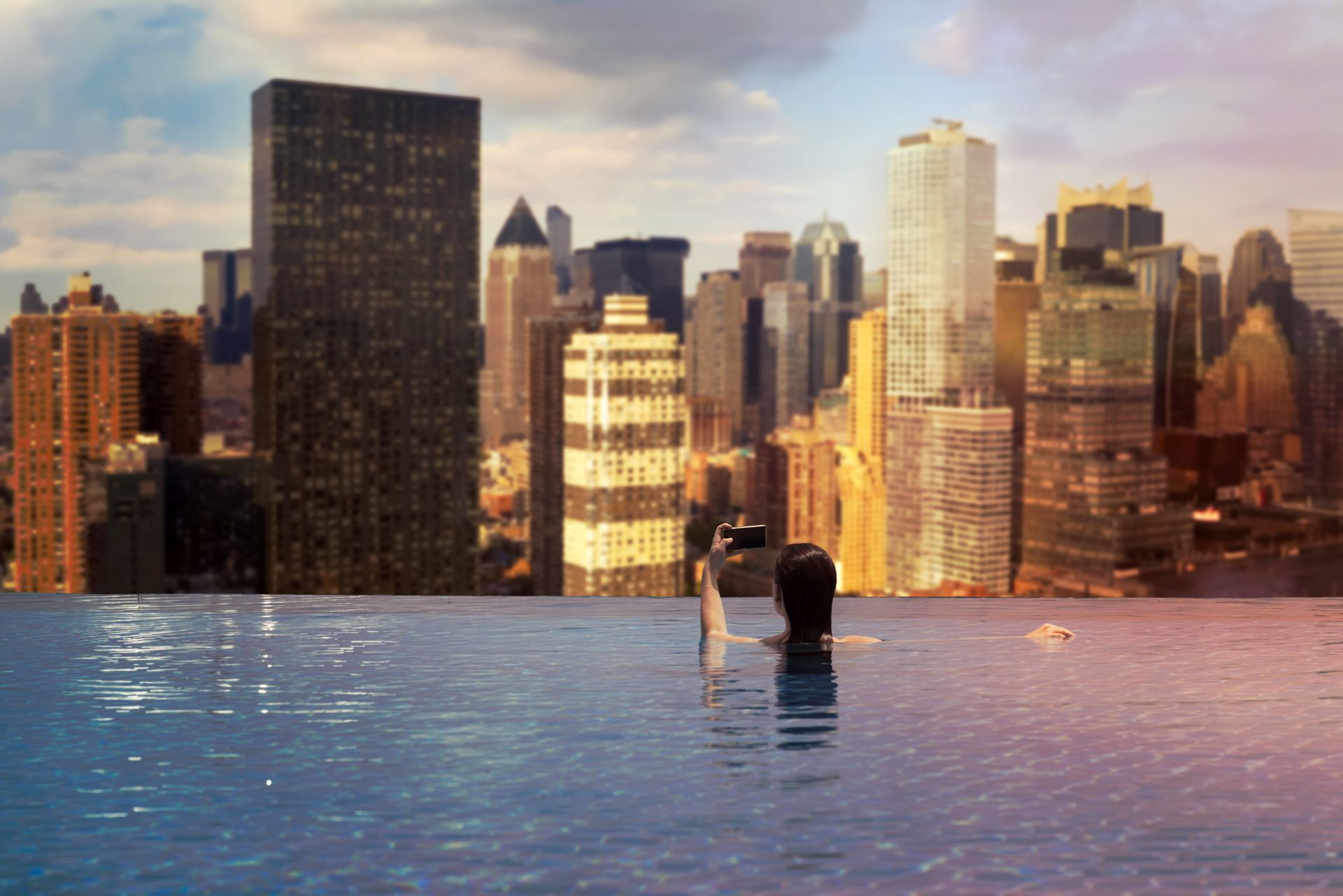 A person is swimming in an infinity pool with a city skyline in the background.