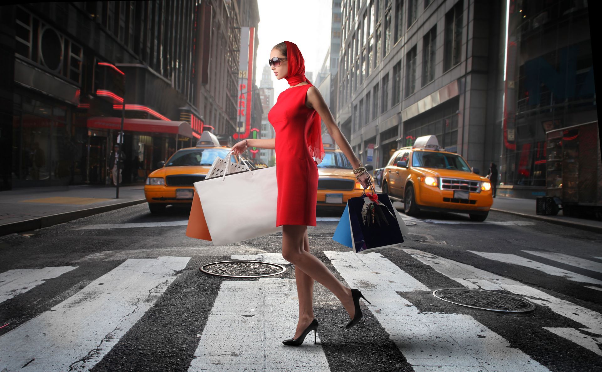 A woman in a red dress is crossing the street with shopping bags