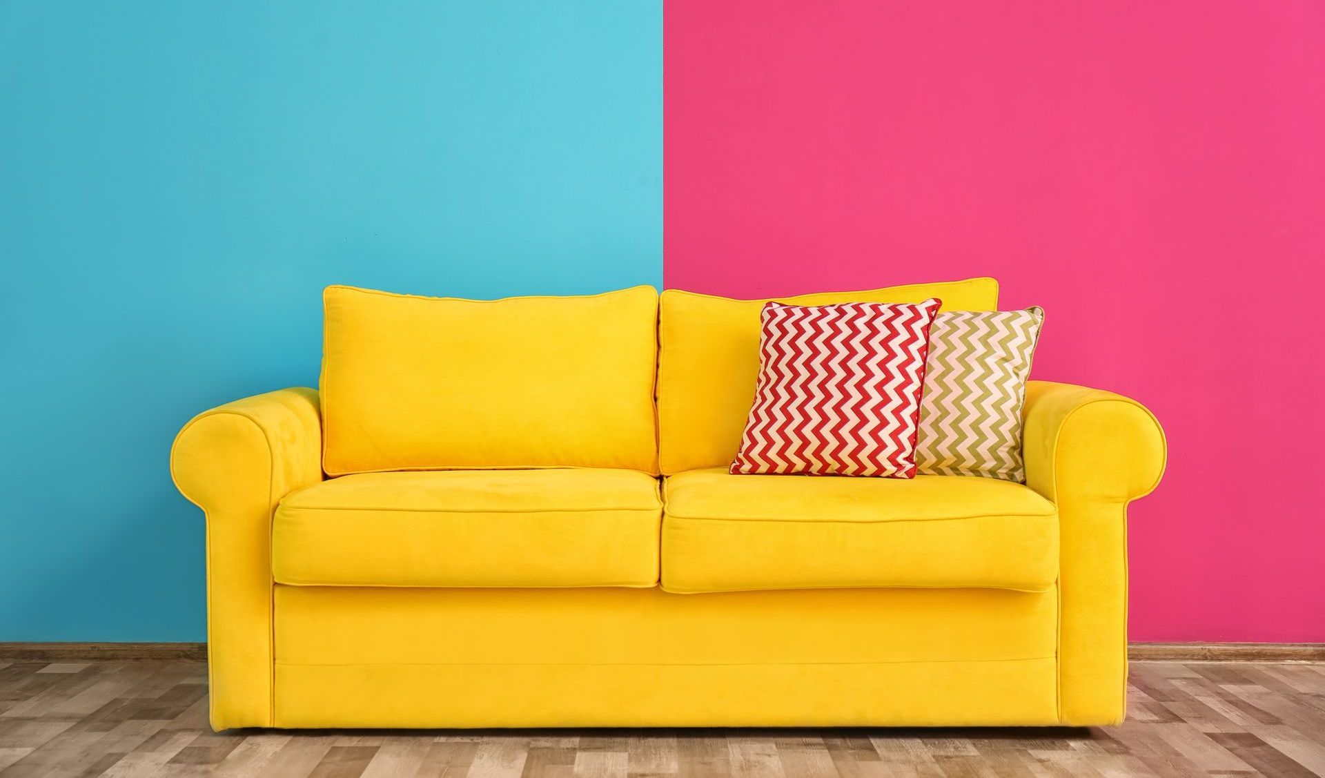 A yellow couch is sitting in front of a pink and blue wall.