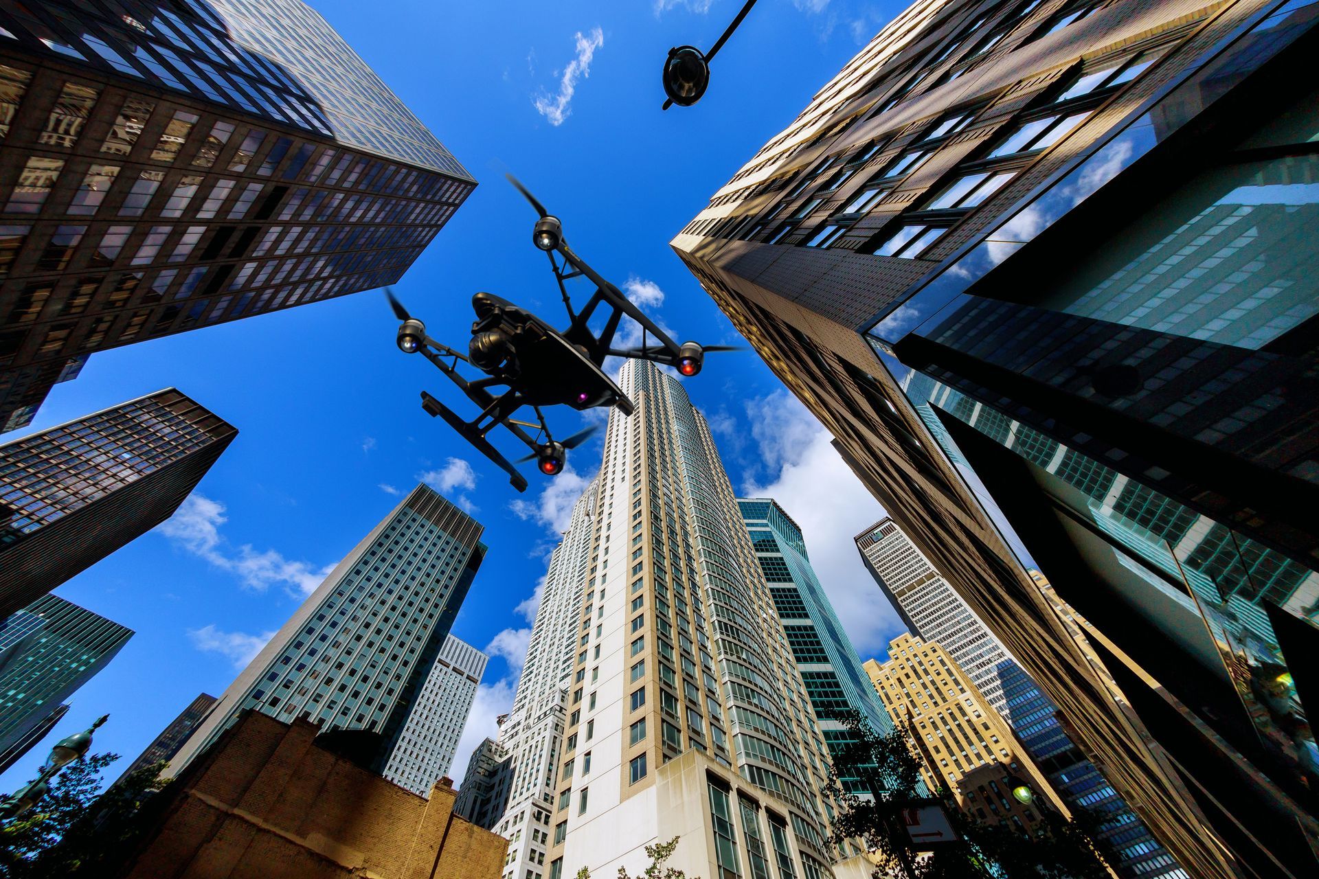 Drone flying amidst skyscrapers under a blue sky. Buildings have varied colors and designs.
