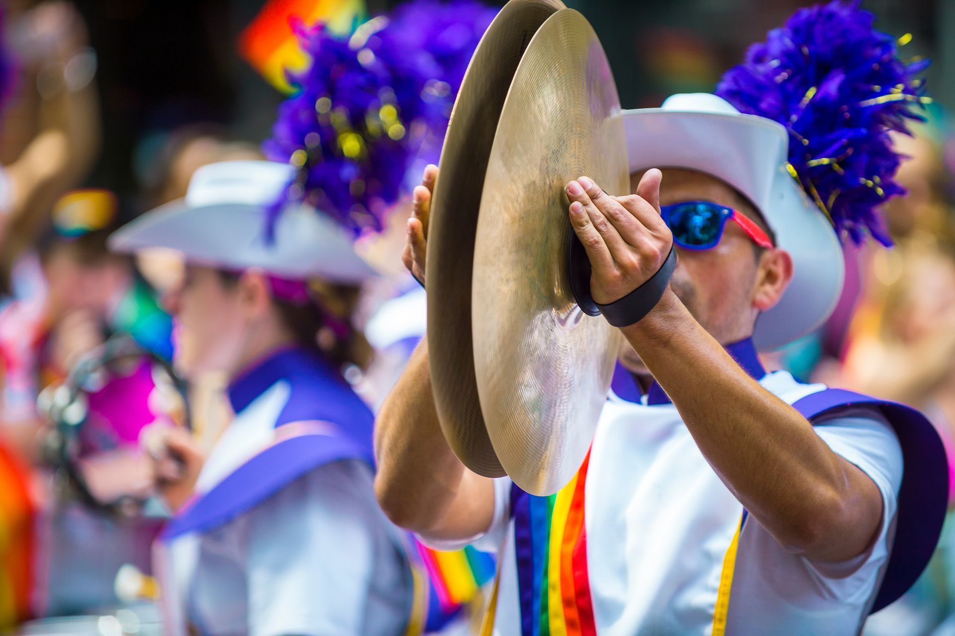 A man in a cowboy hat is playing a cymbal in a parade.