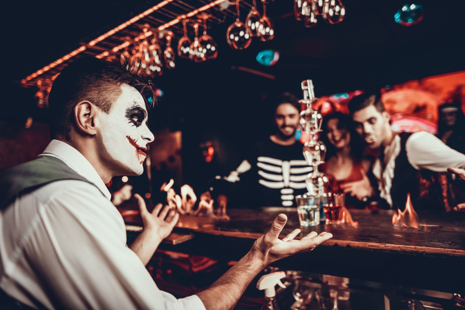 A man in a clown costume is standing at a bar holding a stack of cards.