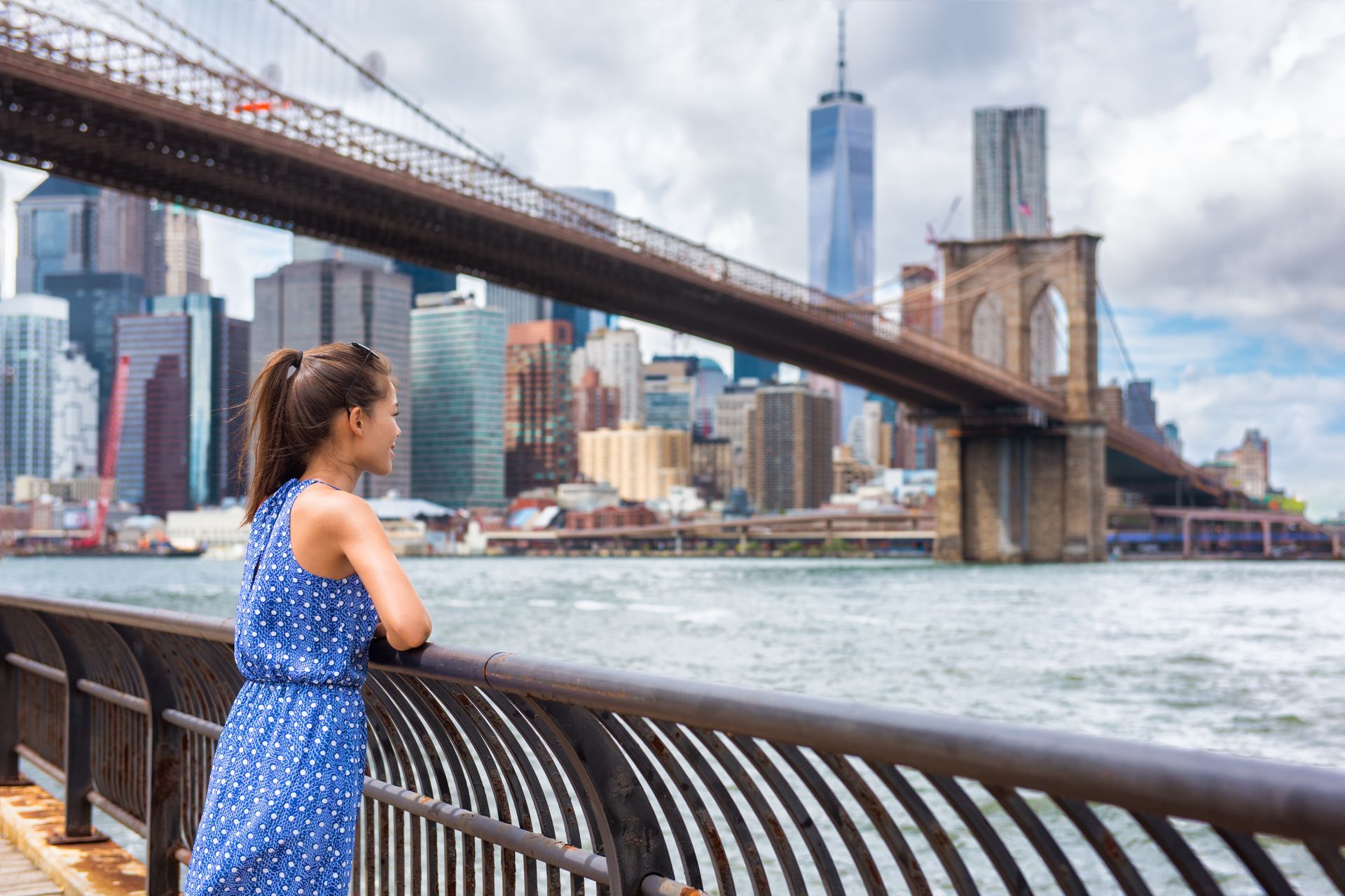 A woman in a blue dress is standing on a bridge overlooking a body of water.