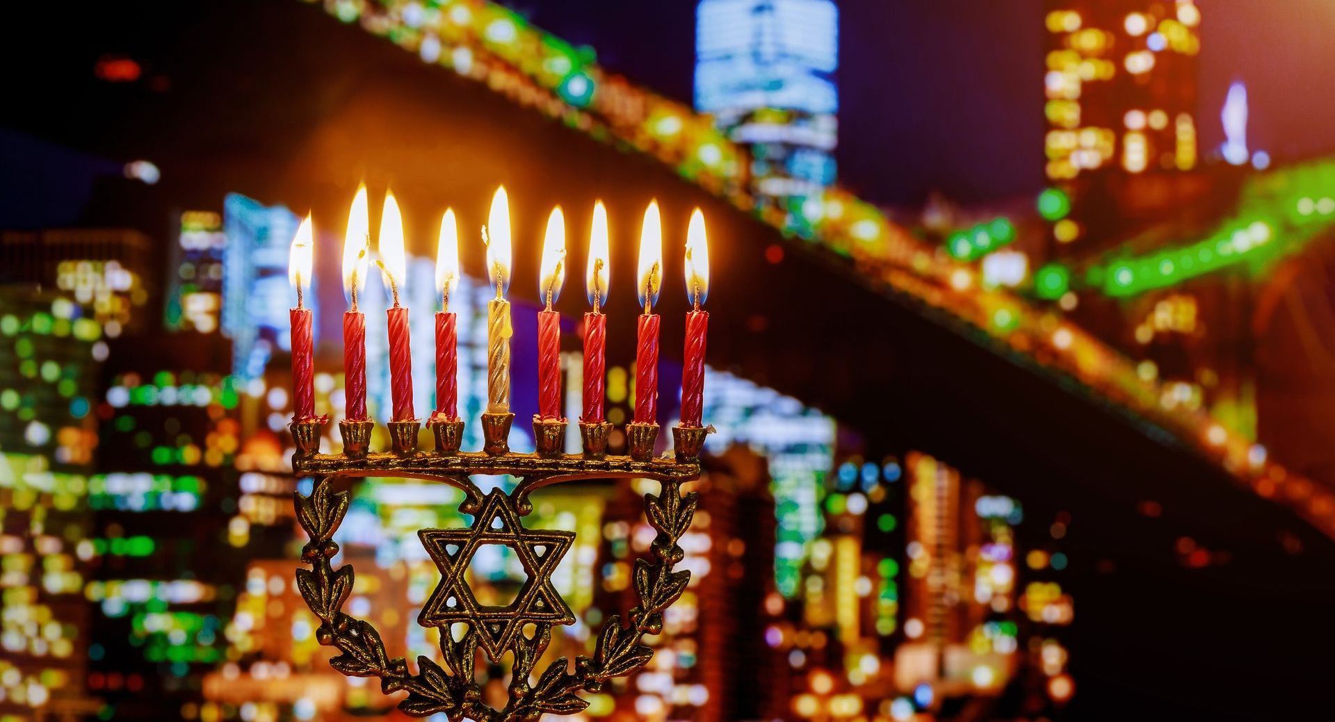 A menorah with lit candles in front of a city skyline at night.