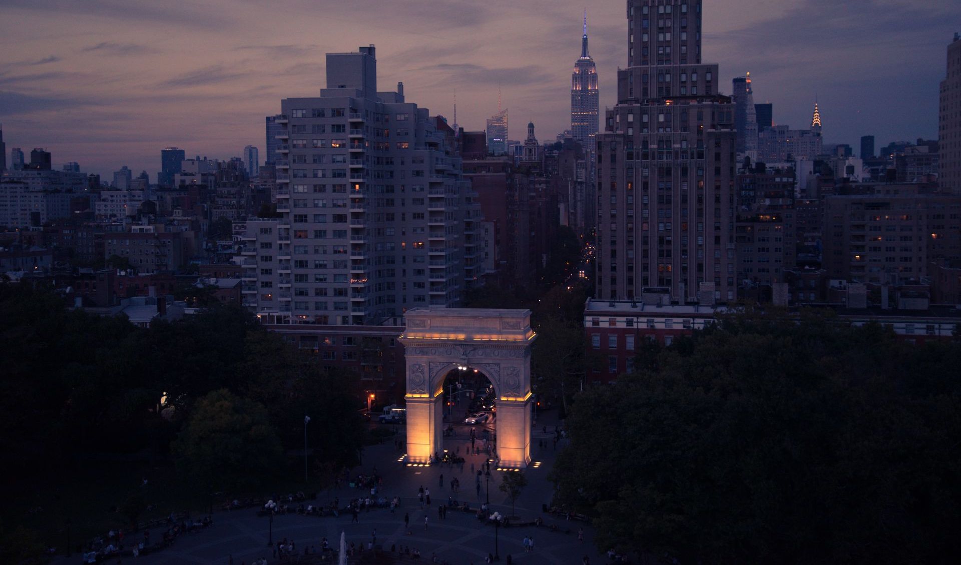Washington Square Arch lit up at dusk, with city buildings in the background.