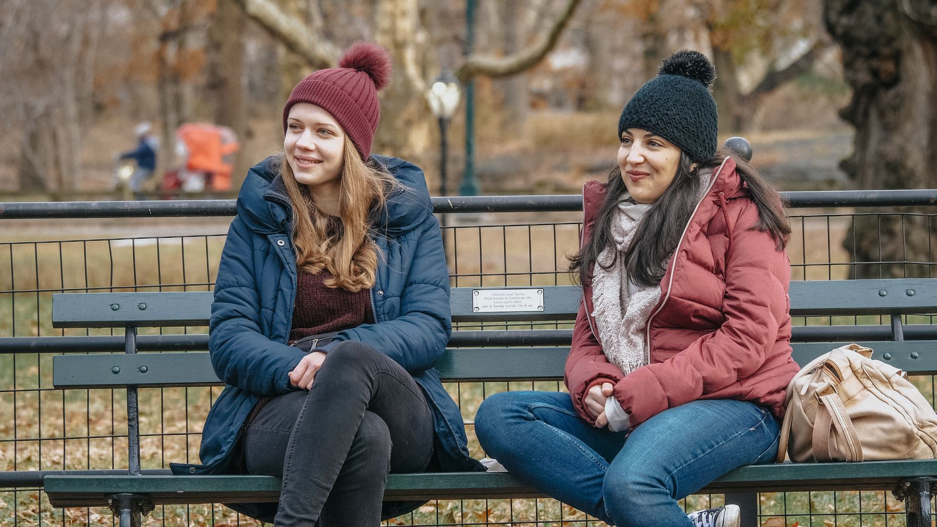 Two women are sitting on a park bench talking to each other.