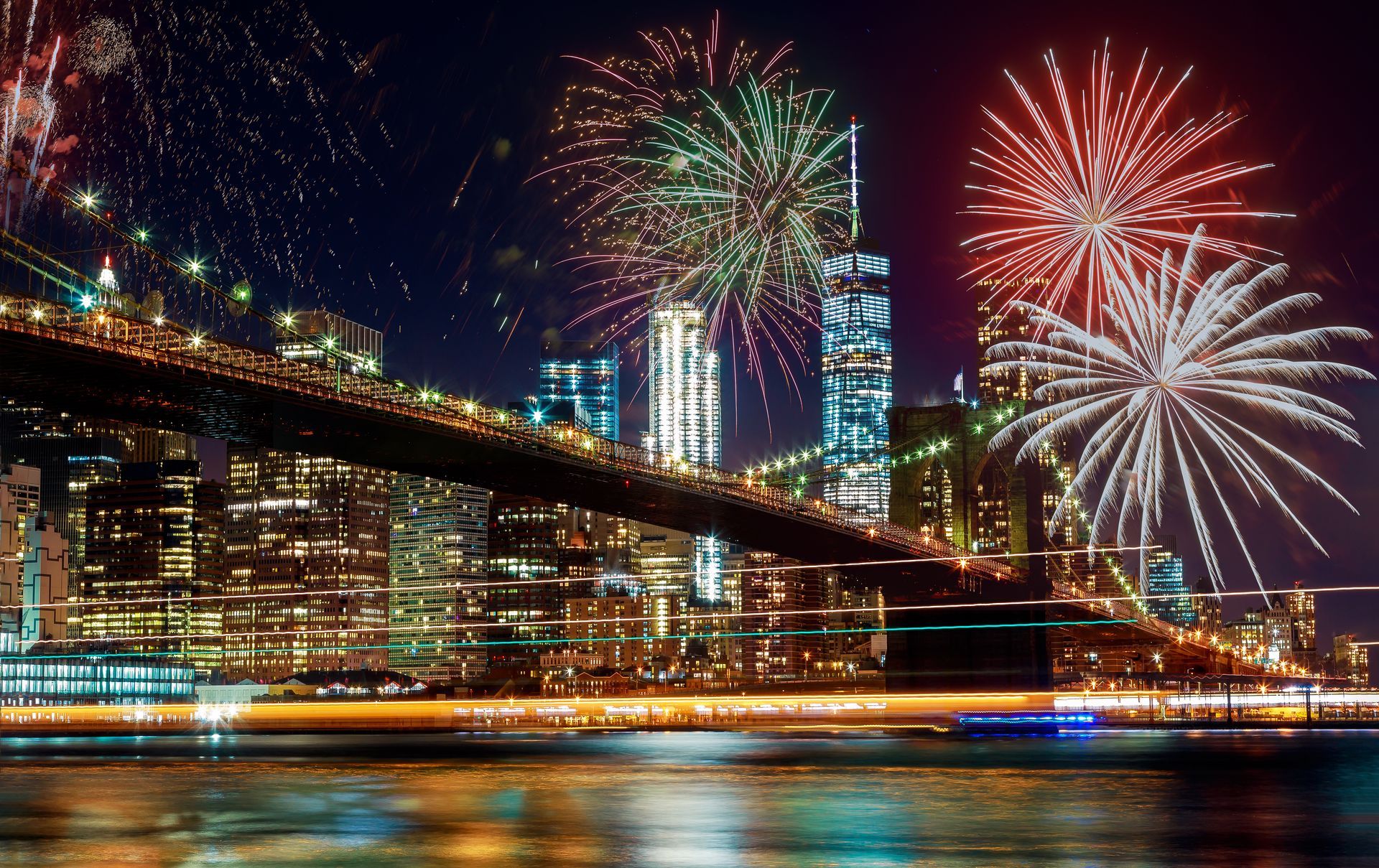 Fireworks are displayed over a bridge over a body of water.