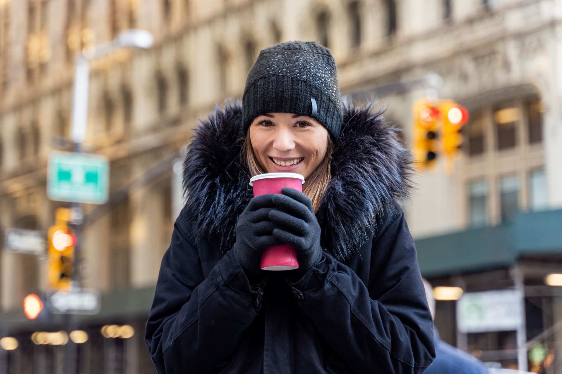 A woman is holding a cup of coffee in her hands on a city street.