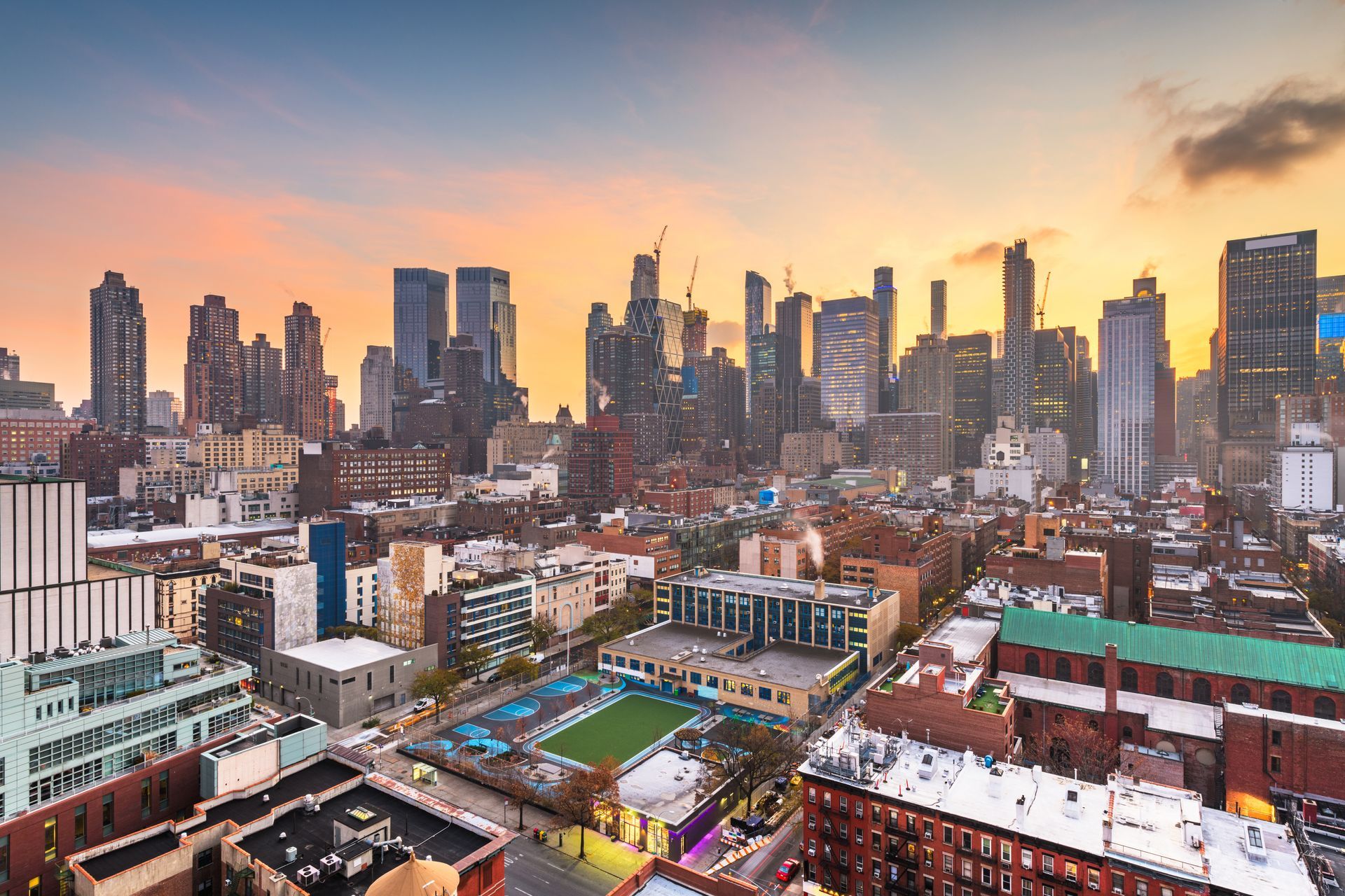 City skyline at sunset with tall buildings and a few construction cranes.