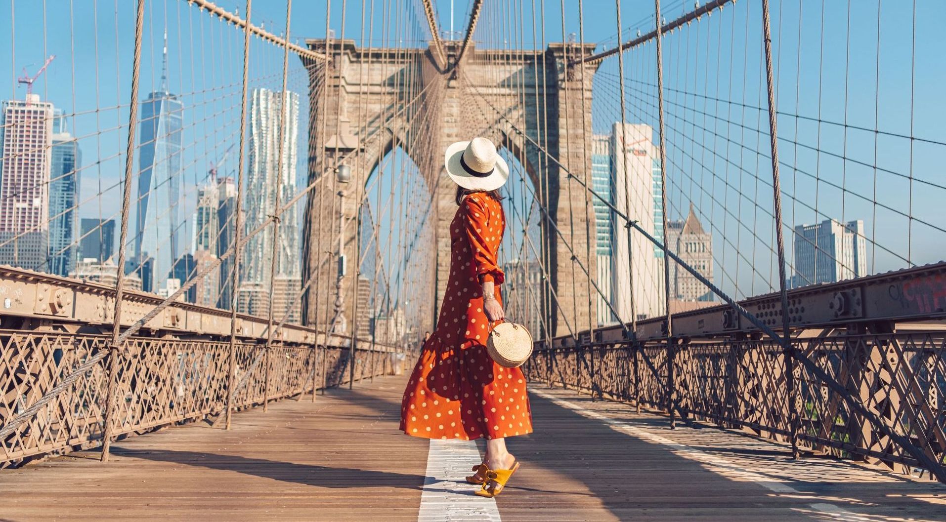 A woman in a red dress and hat is walking across a bridge.