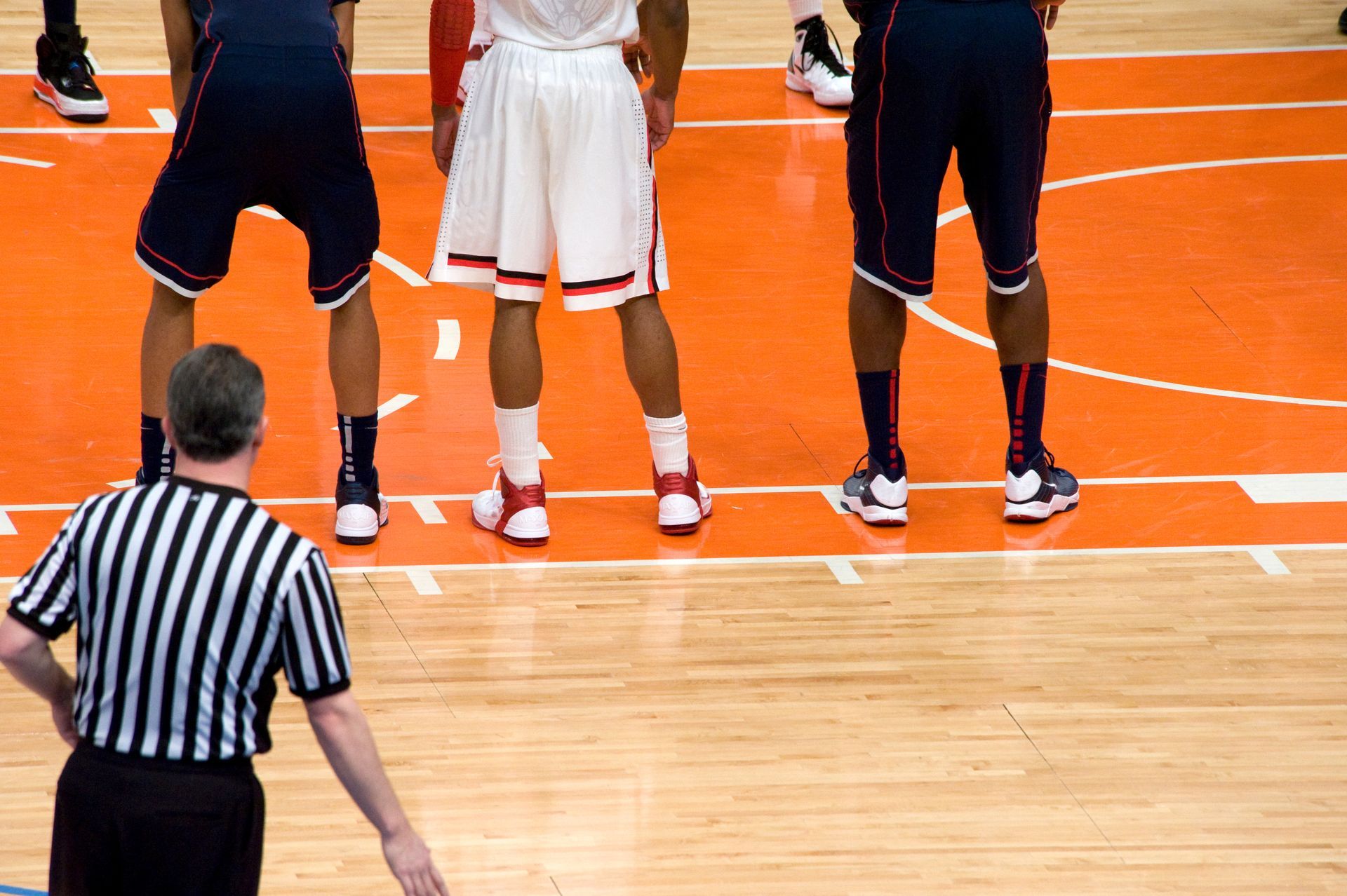 A referee stands on a basketball court with basketball players in the background