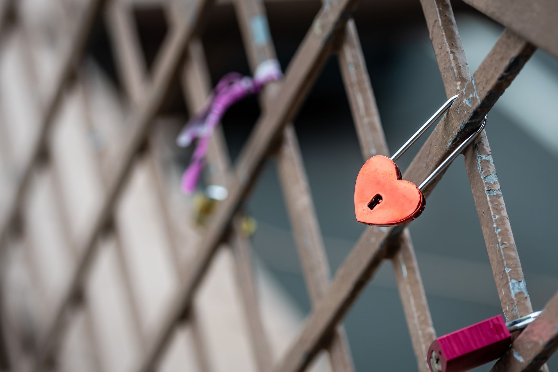 Heart-shaped orange padlock locked to a metal fence with other locks in the background.