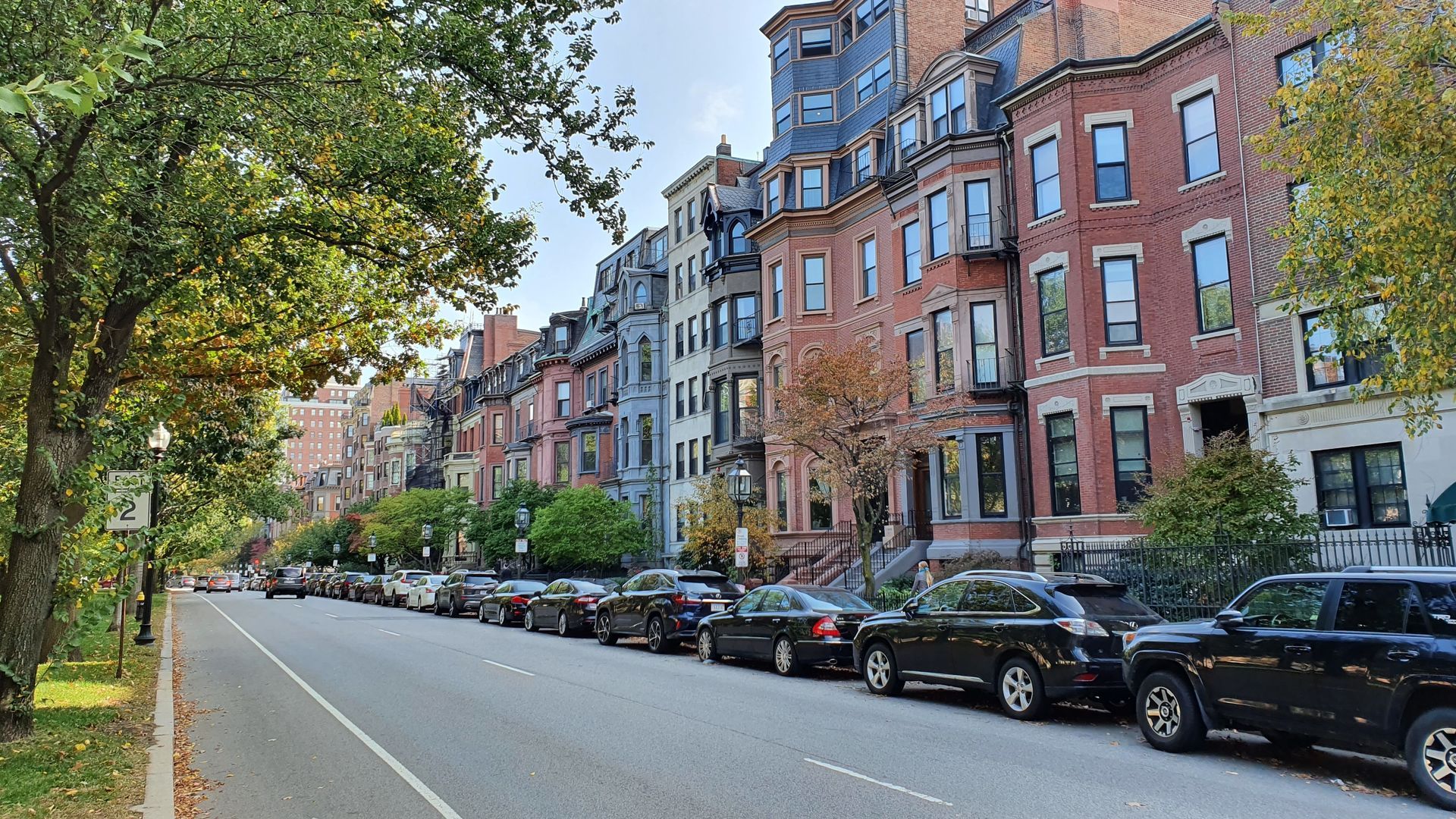 Street view of colorful brick row houses in Boston, Massachusetts, with parked cars and trees.