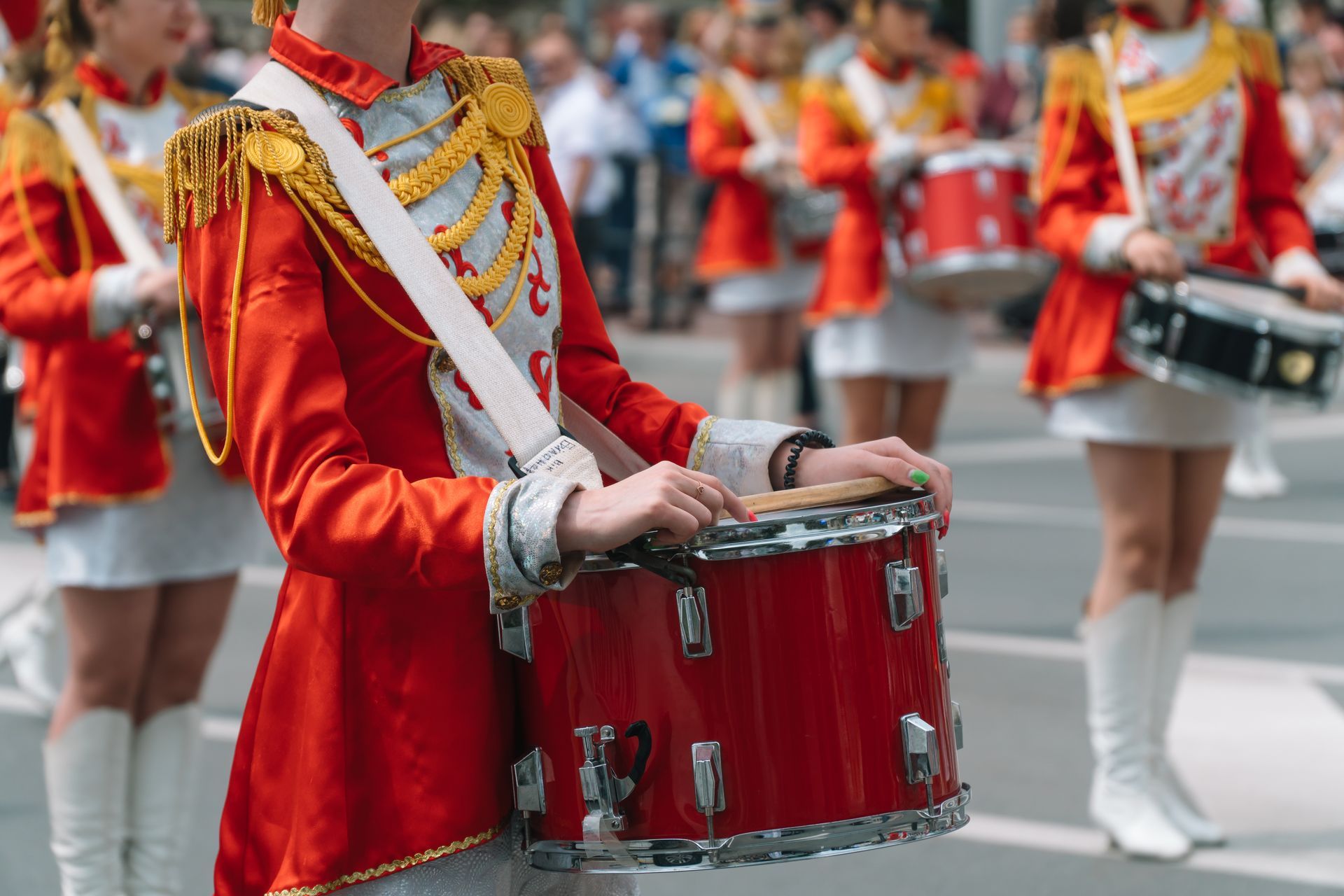 A group of marching band members are walking down the street holding drums.