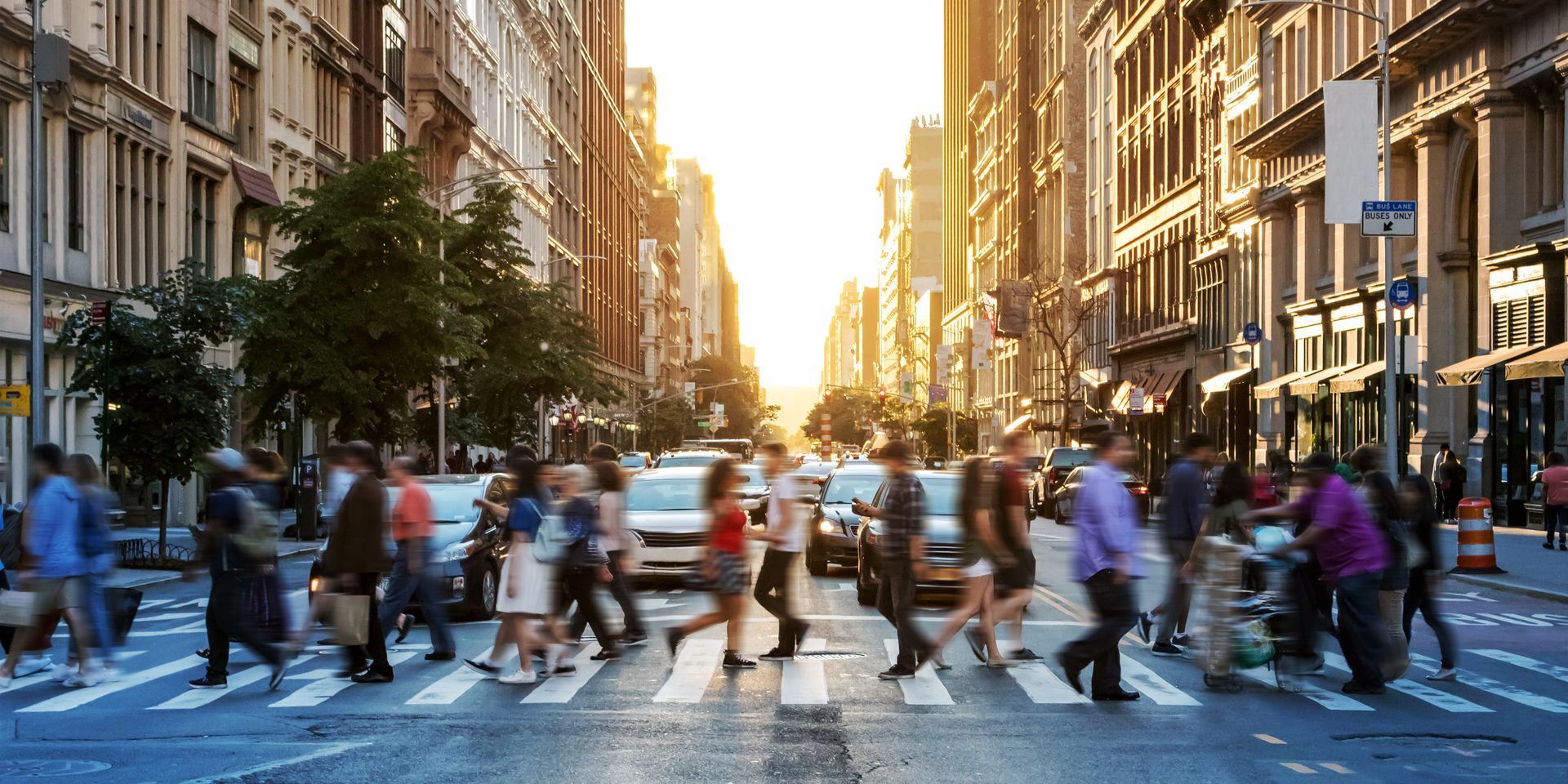 A large group of people are crossing a city street at a crosswalk.