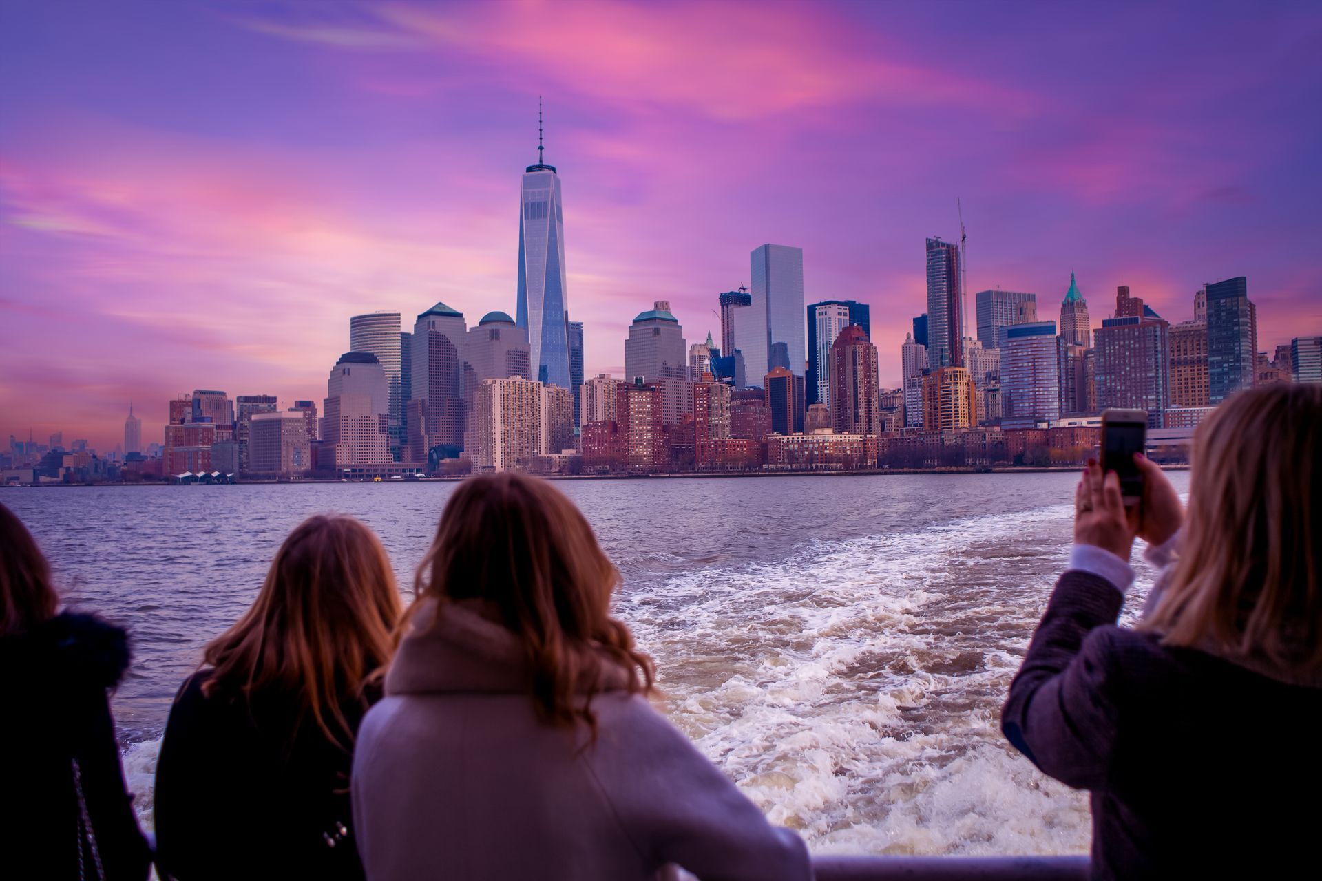 A group of people are taking a picture of the city skyline from a boat.