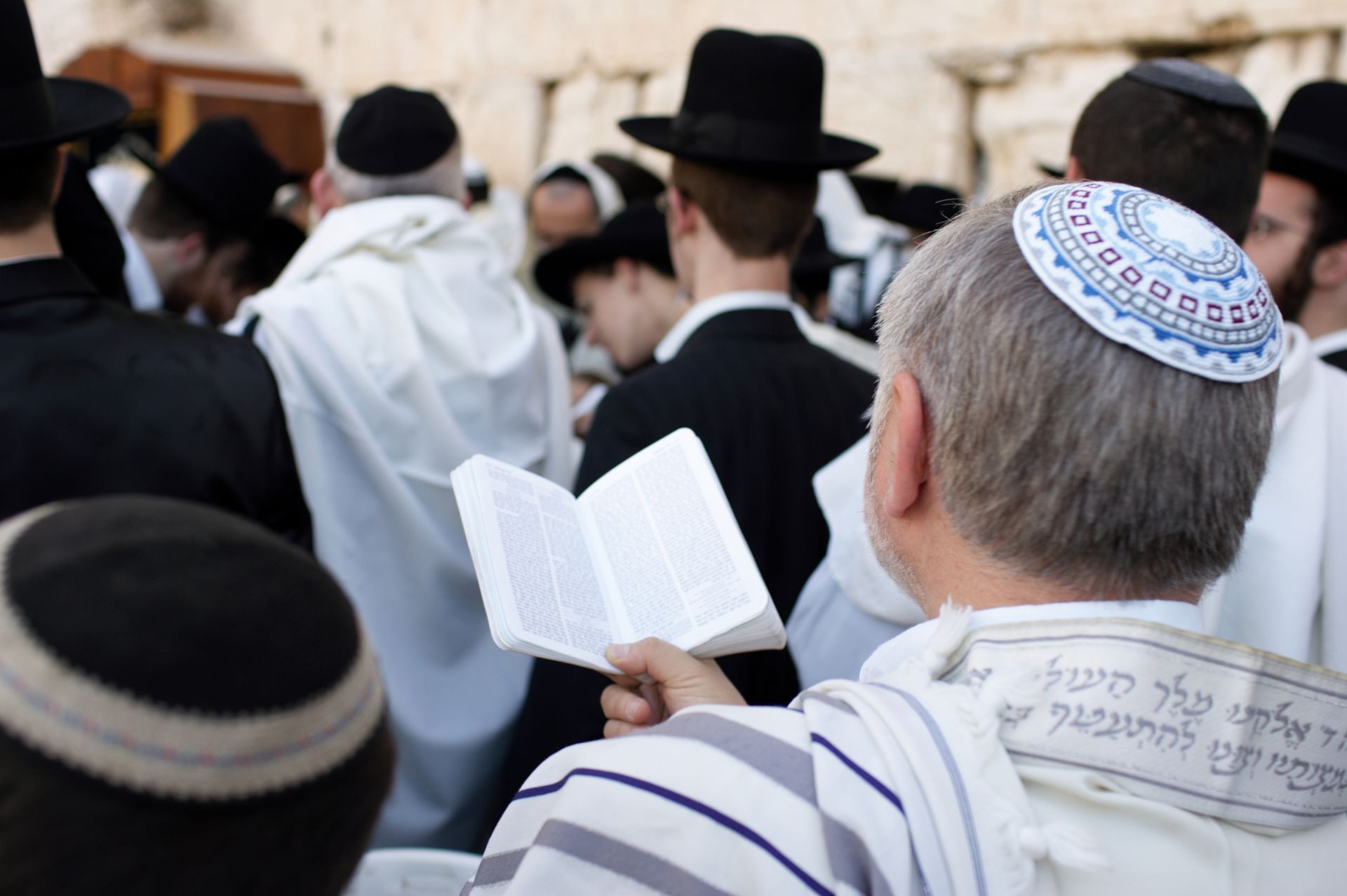 A man wearing a kippah is reading a book