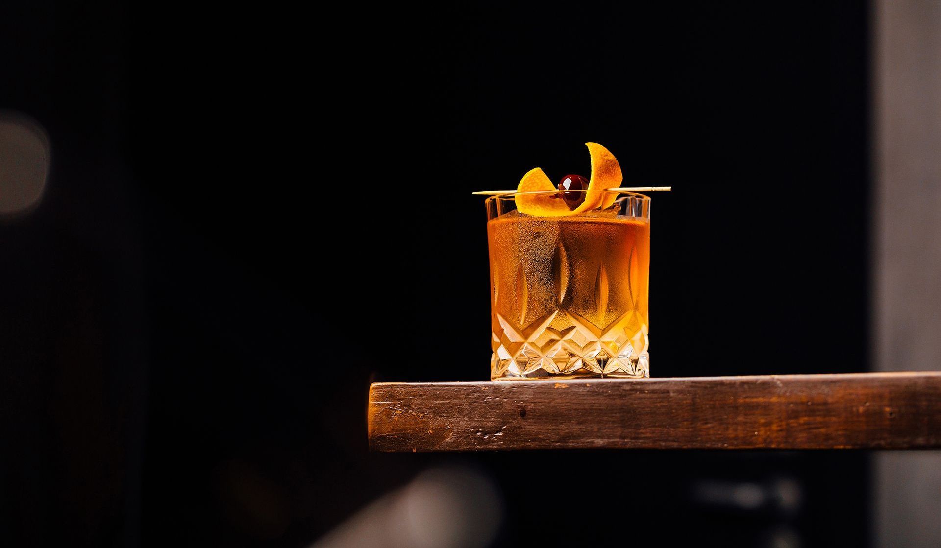 a close up of a whiskey old fashioned on a wooden shelf .