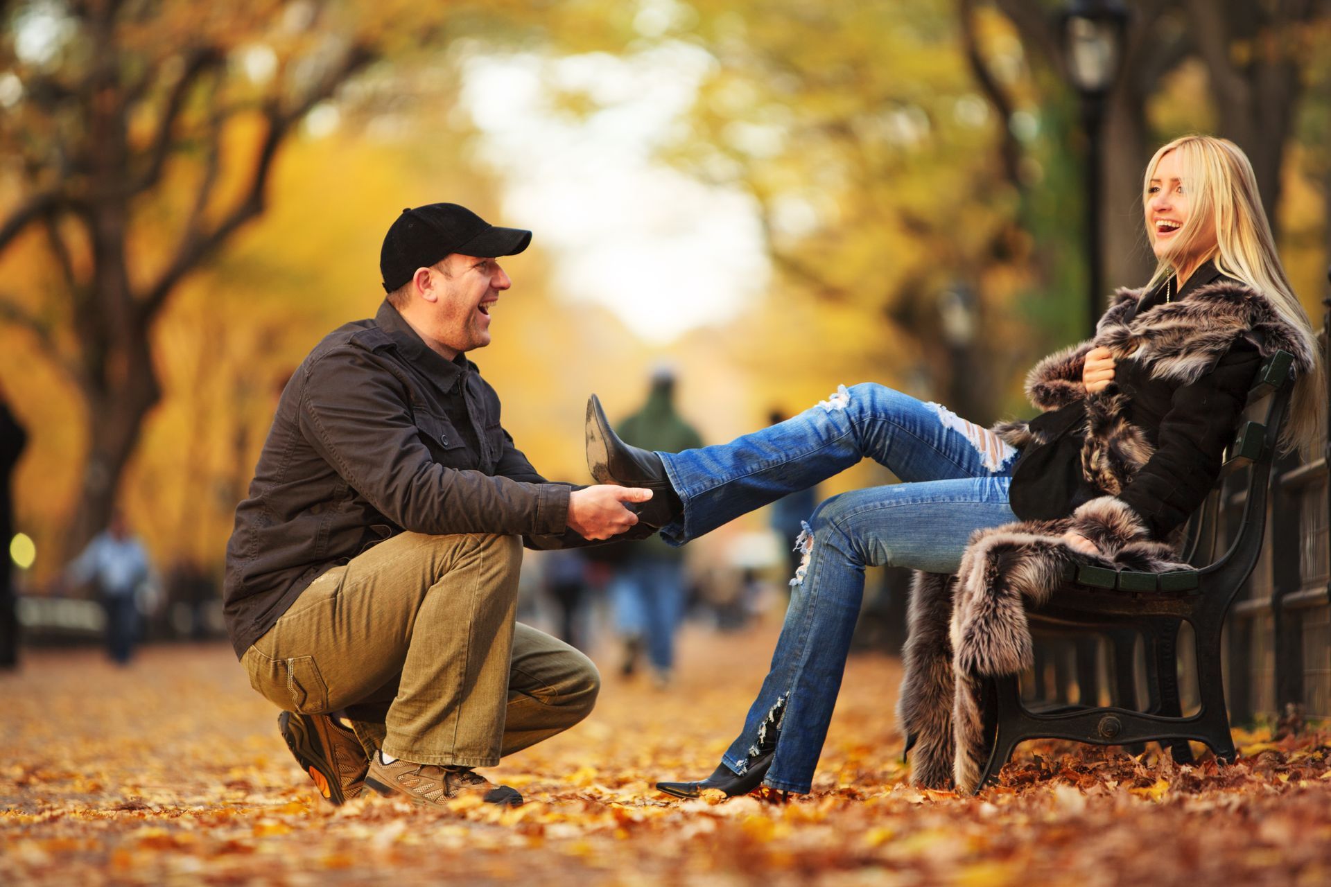 A man is kneeling down next to a woman sitting on a park bench.