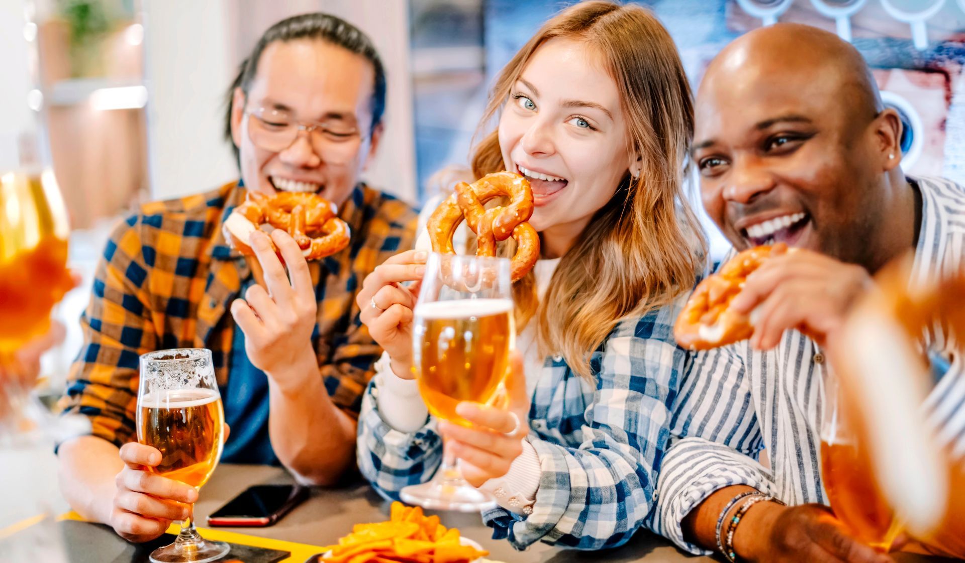 A group of people are sitting at a table eating pretzels and drinking beer.