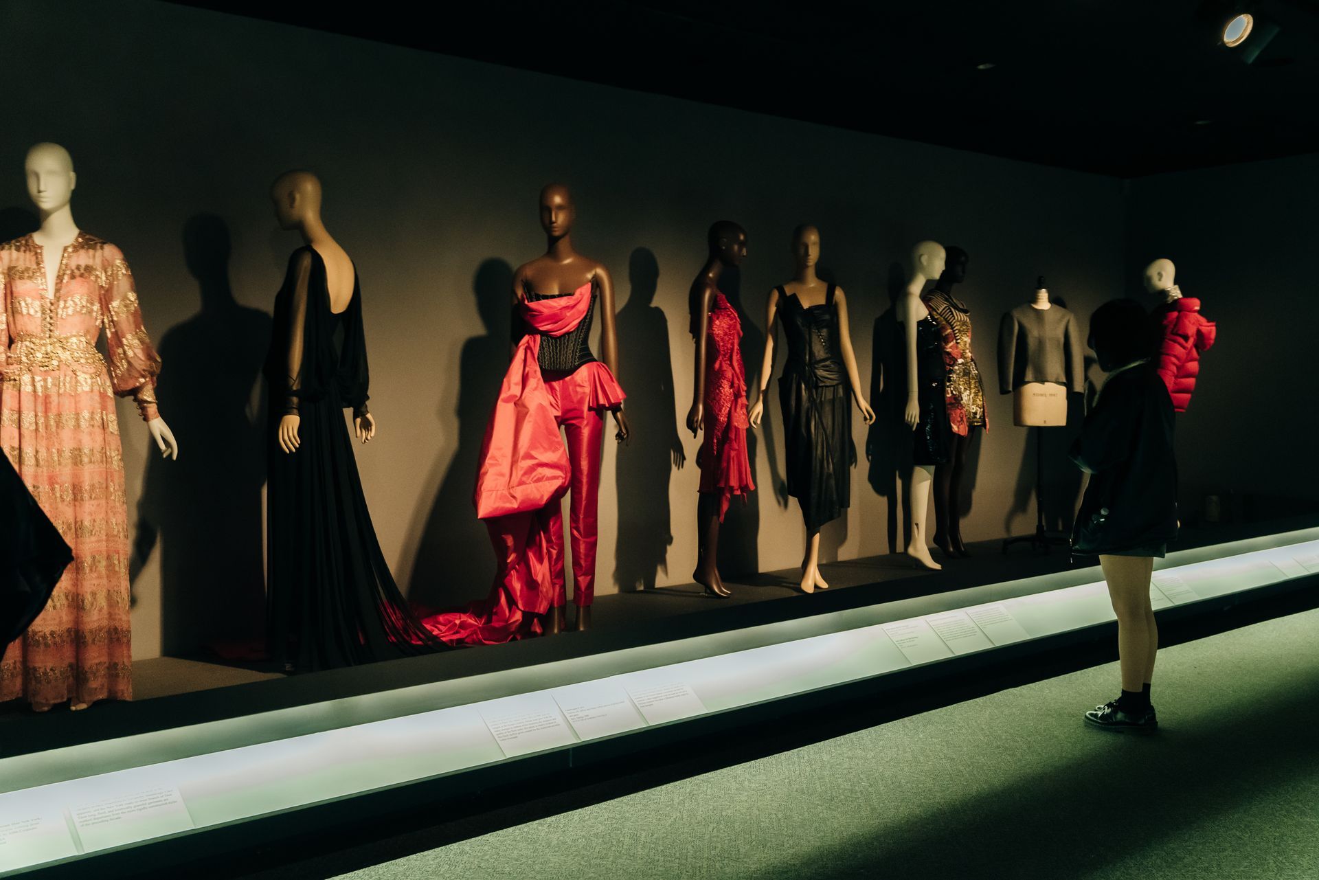 Fashion display at museum: mannequins in elegant gowns, one person viewing exhibit.