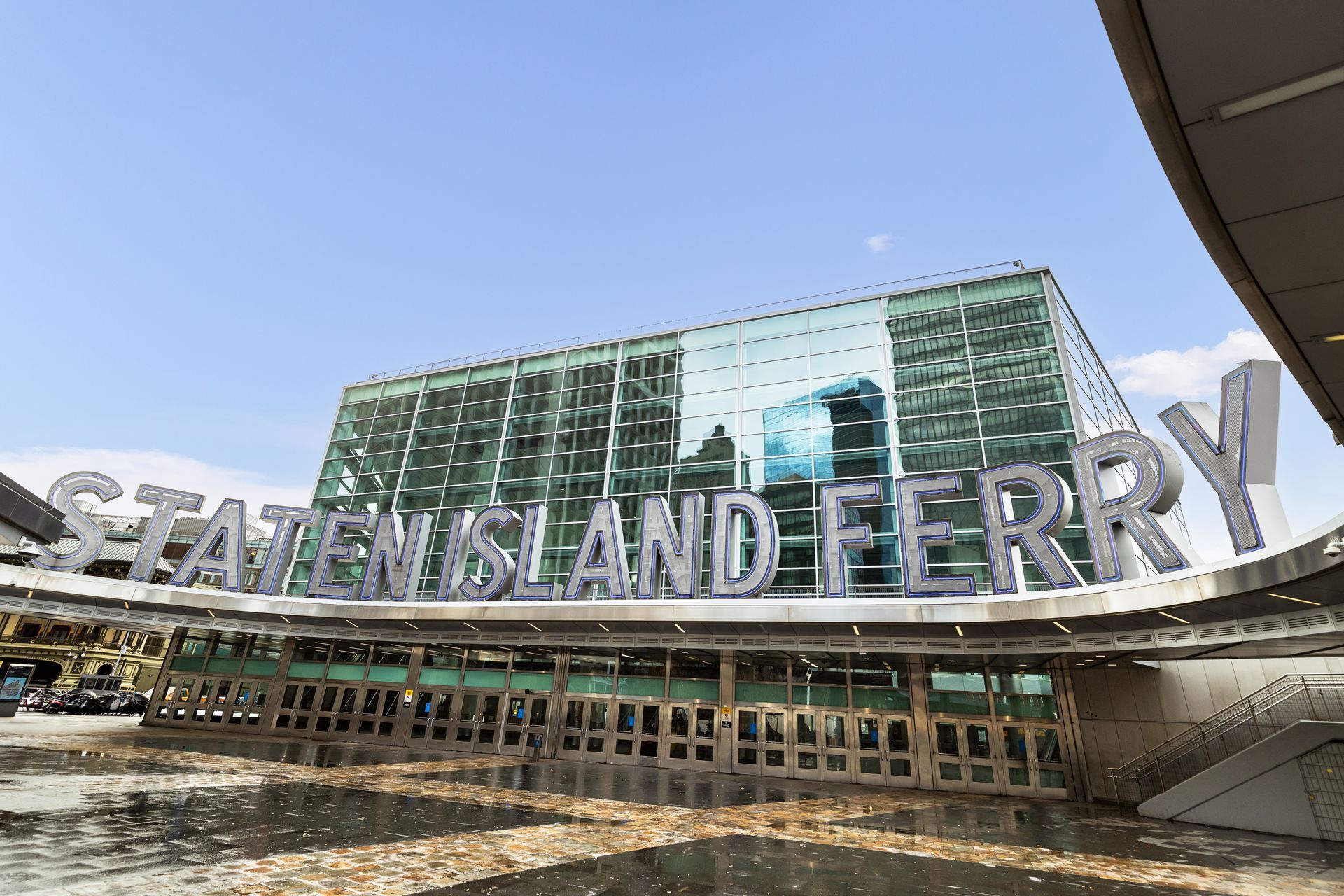 Staten Island Ferry terminal entrance with large sign under a blue sky.