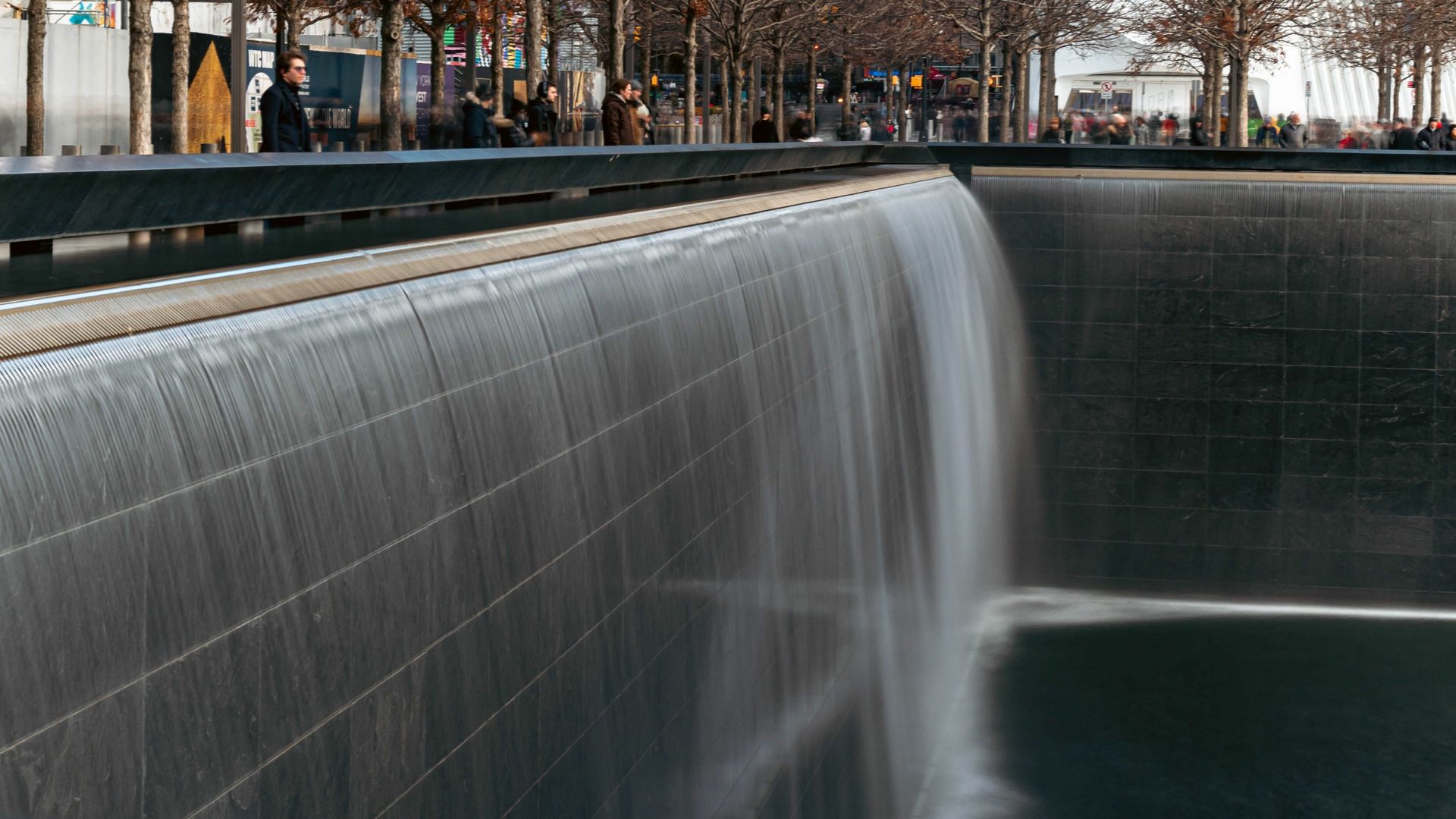 A waterfall is surrounded by a brick wall and people are walking around it.