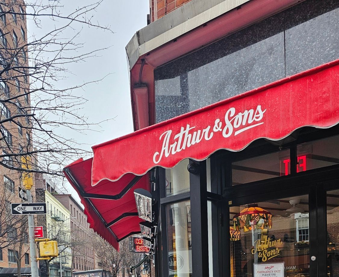 A red awning on the side of a building that says arthur & sons