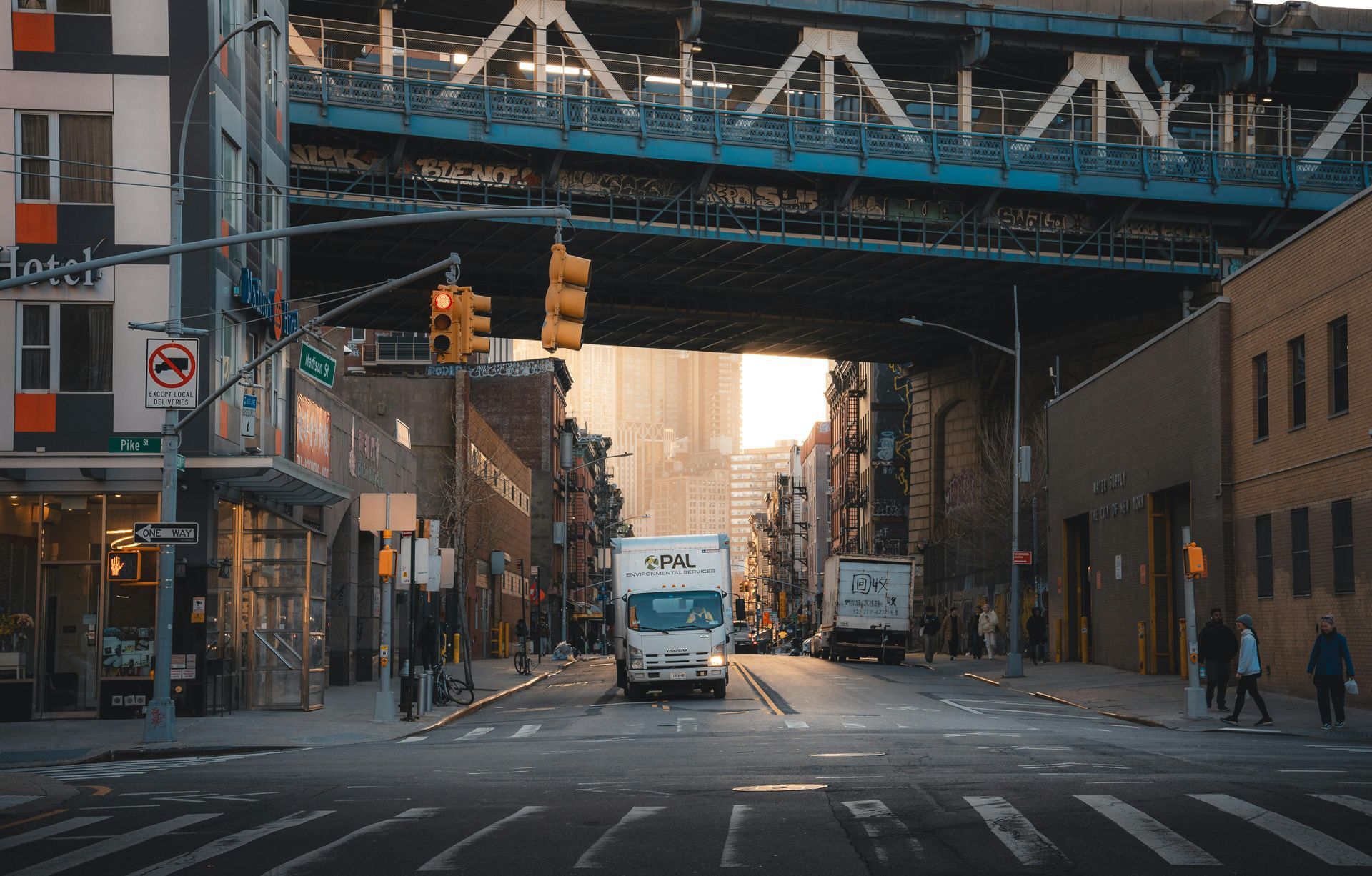 City street scene with bridge overhead. A white truck drives towards the camera.