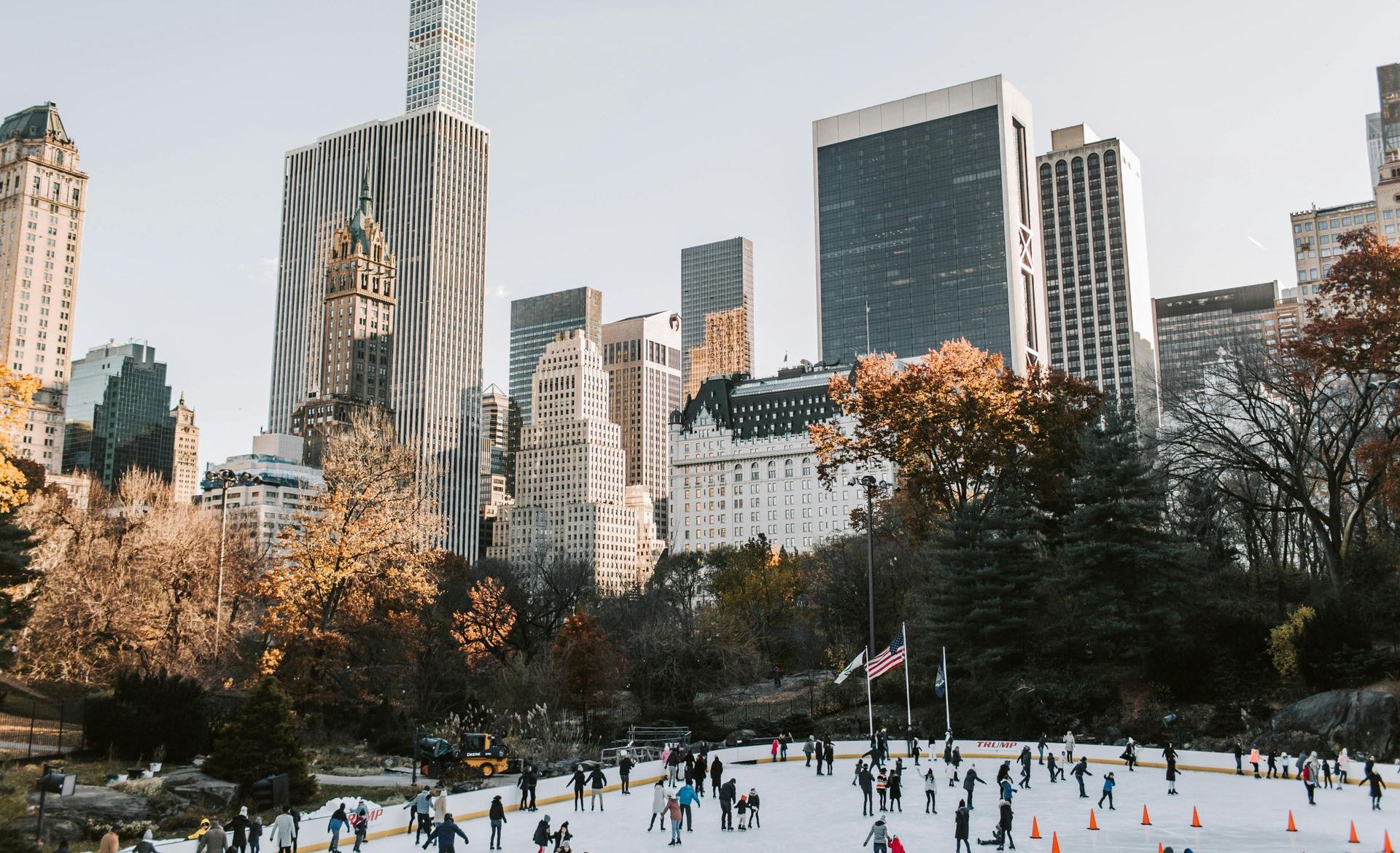 A group of people are ice skating in a park in front of a city skyline.