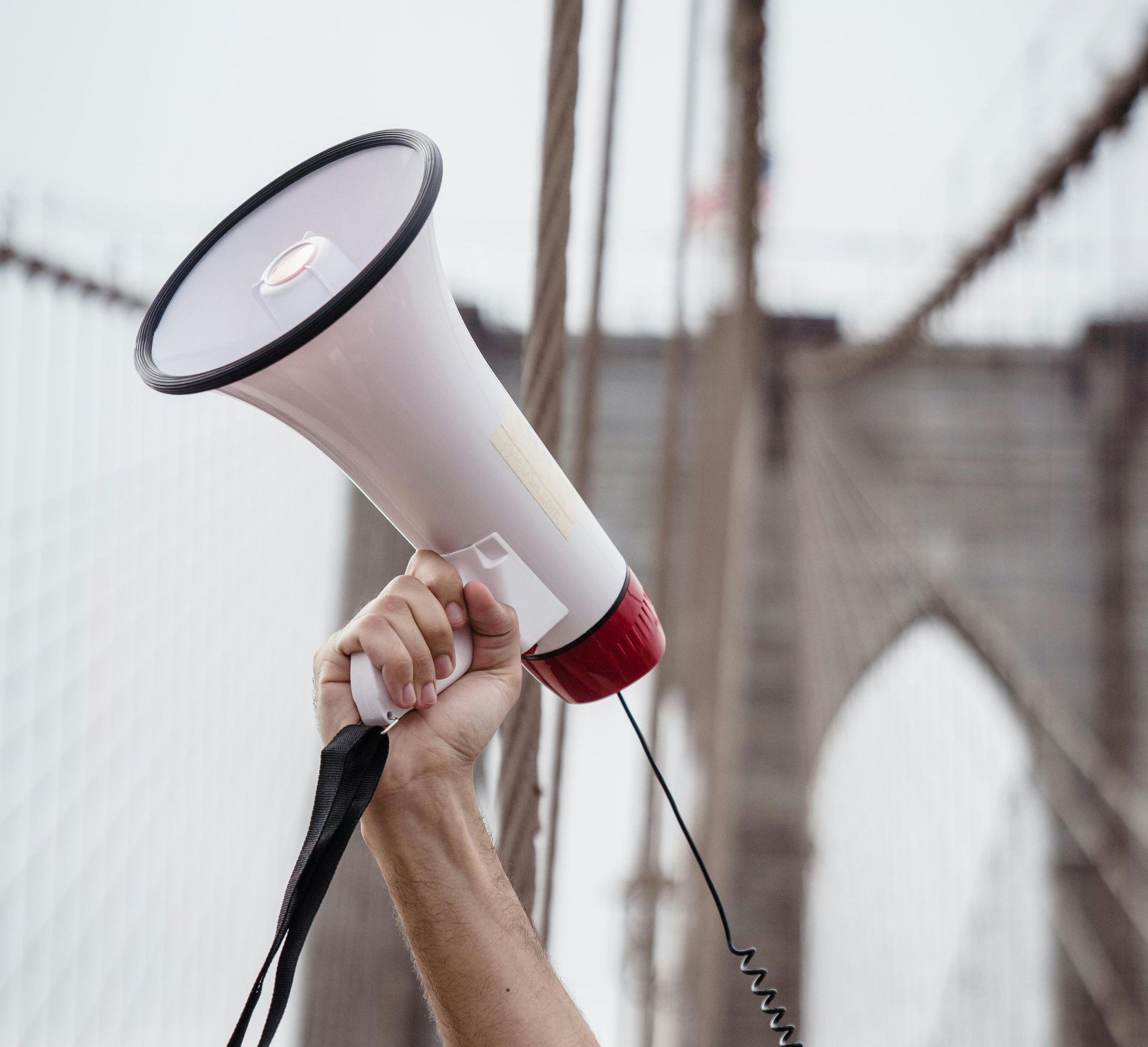 A man is holding a megaphone in front of a bridge.