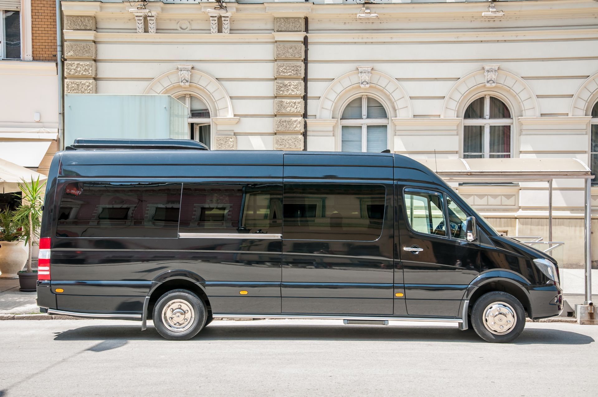 White passenger van parked at an airport. People with luggage stand nearby.