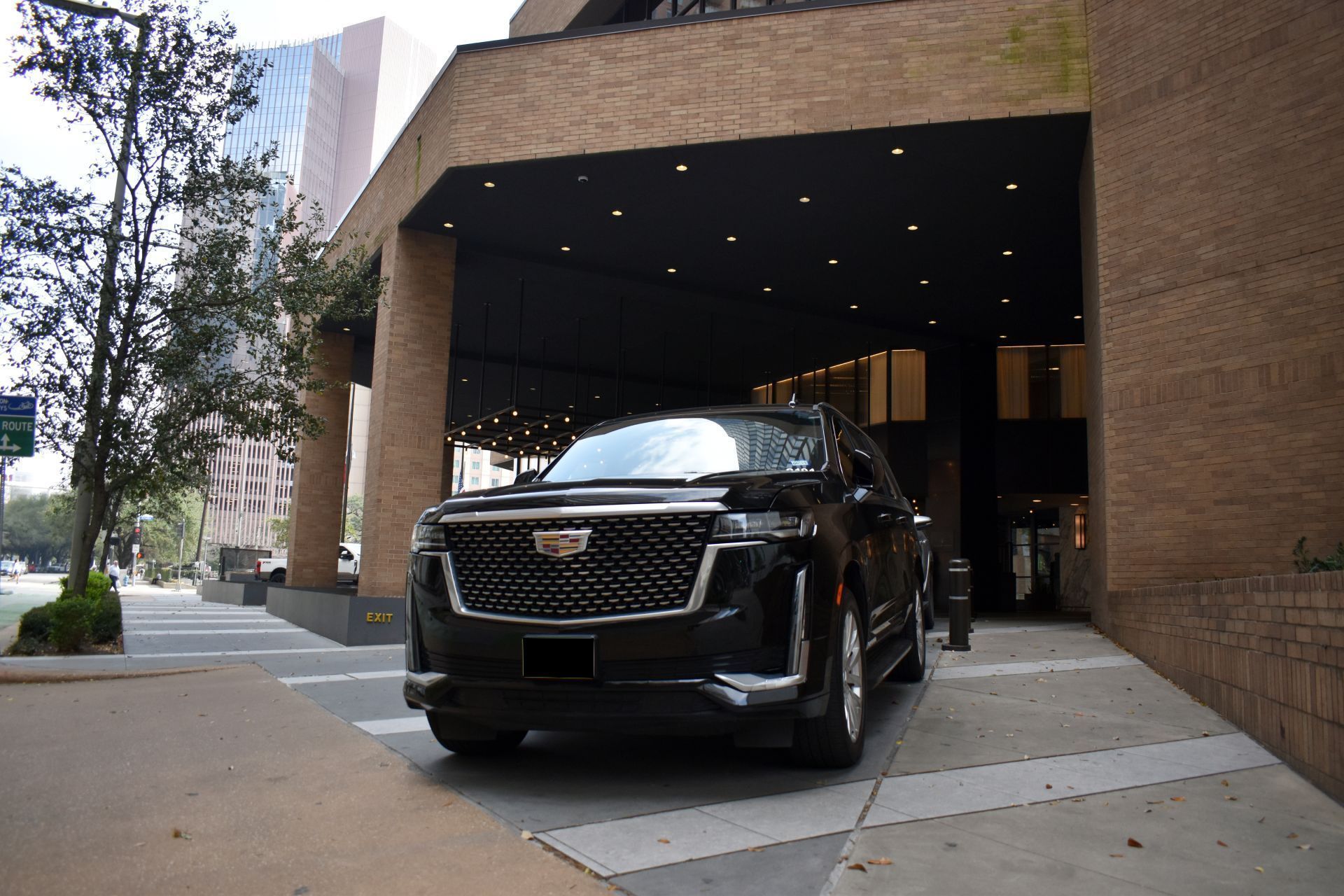 Black Cadillac SUV parked under a covered entrance of a brick building.