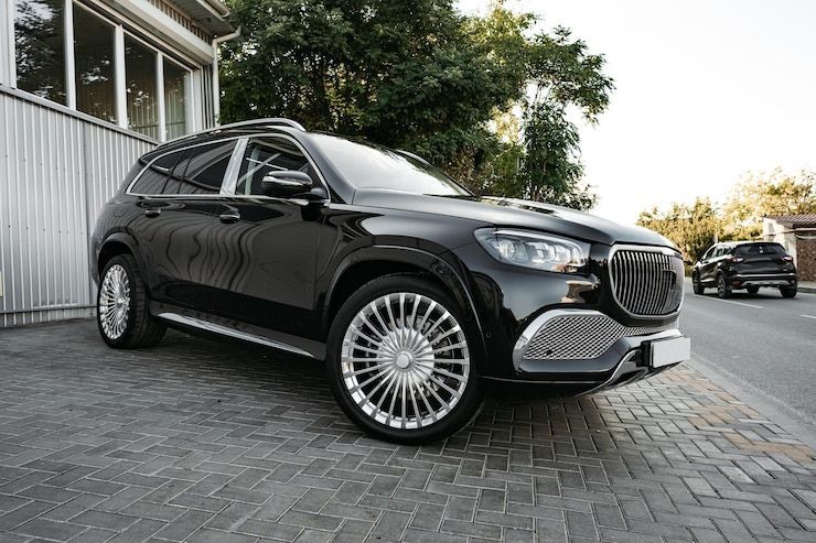 Black SUV parked on brick. Silver rims and grille, shiny exterior. Another vehicle in background.