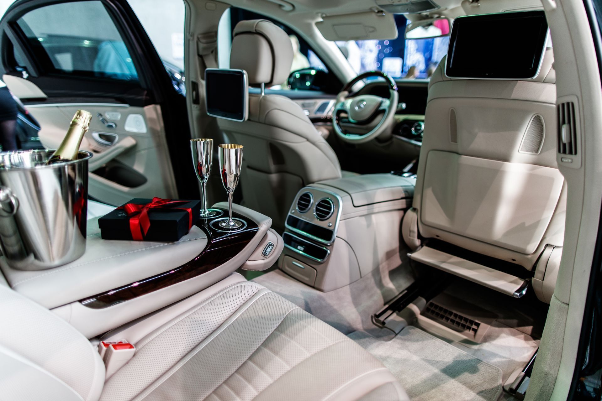 Luxurious car interior: cream leather seats, champagne bucket, gift box, and two flutes on a console.