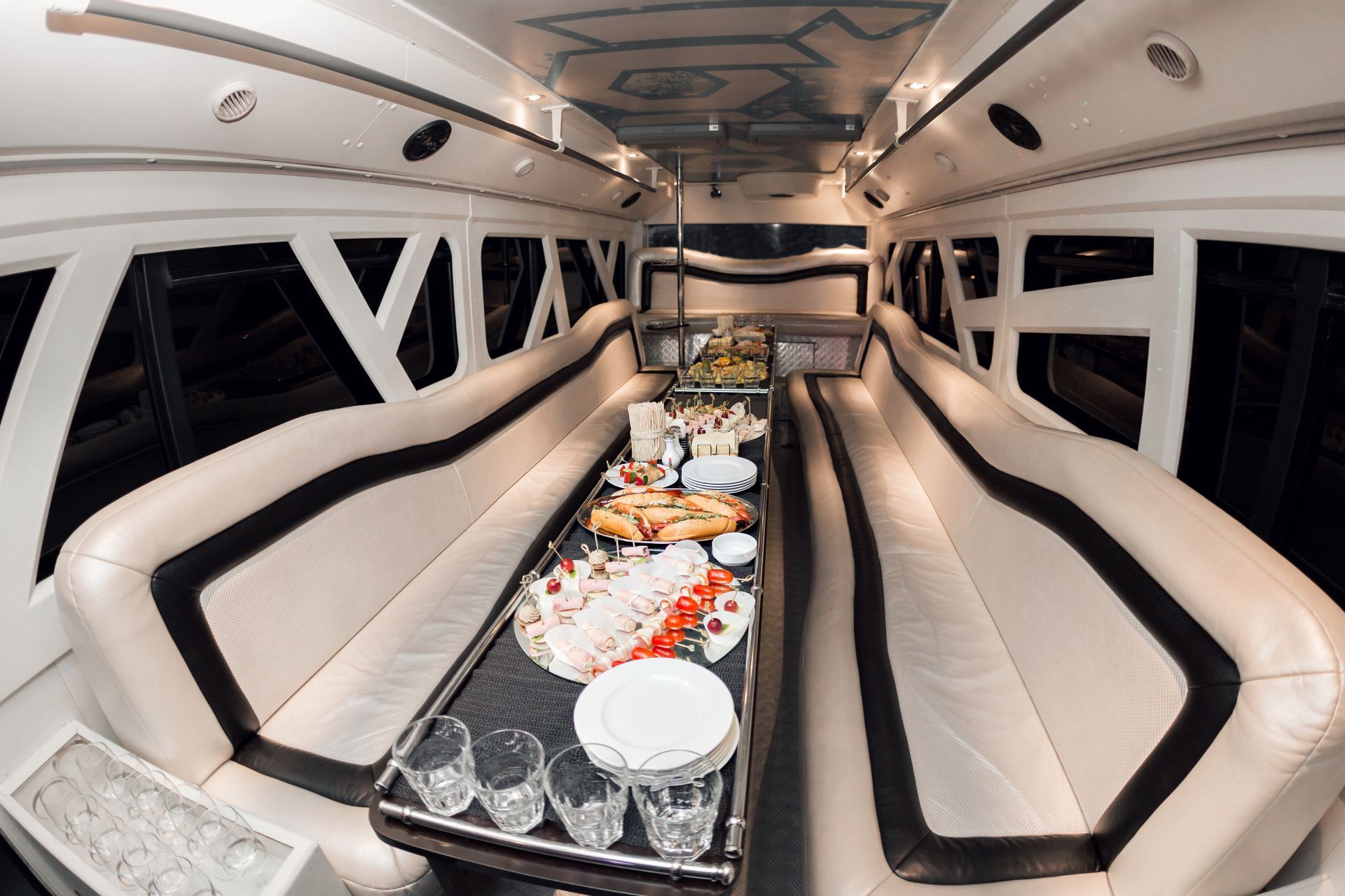 Interior of a luxury limo with white leather seating, a table with snacks and drinks.