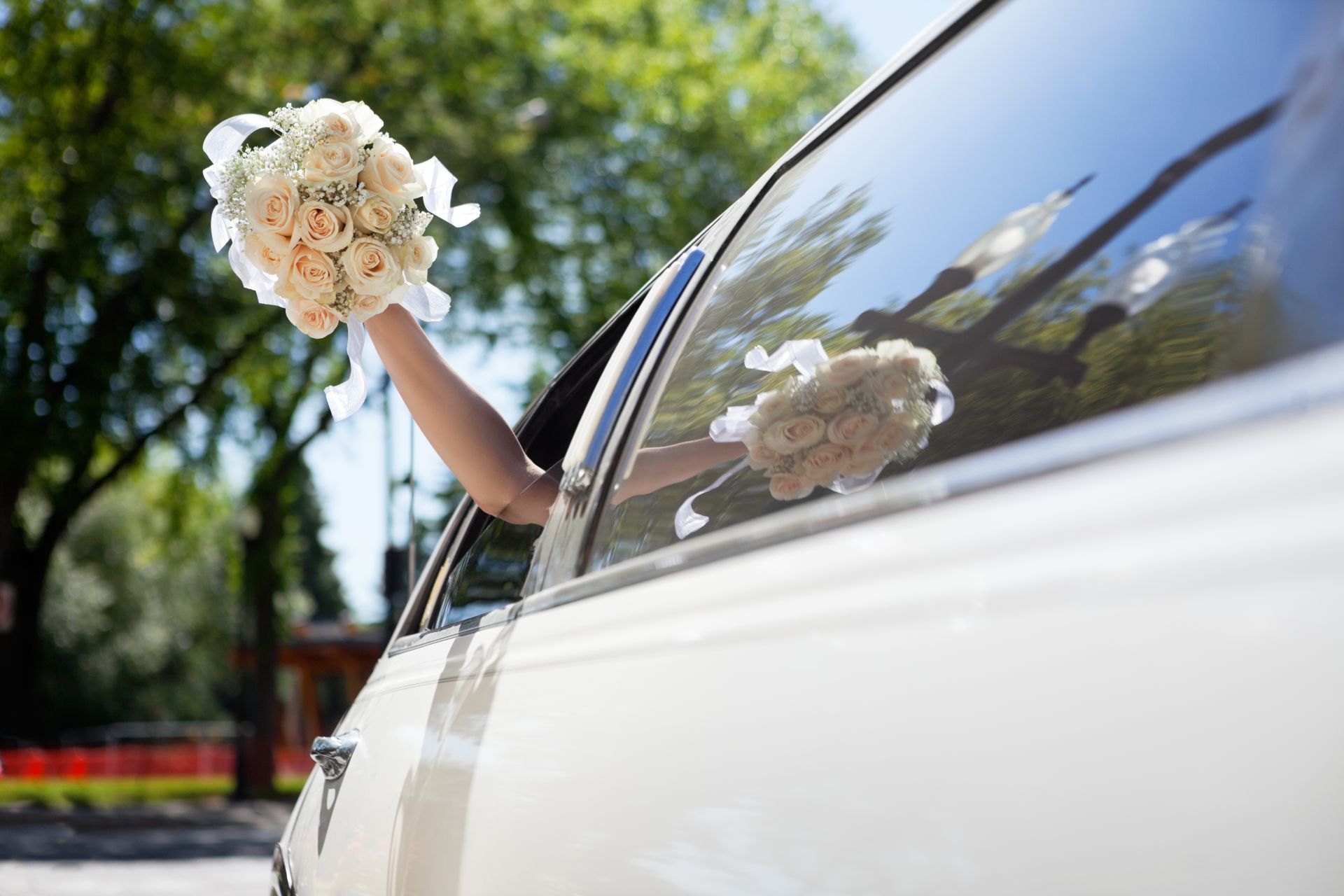 Person in a white car waving a bouquet of flowers out the window.