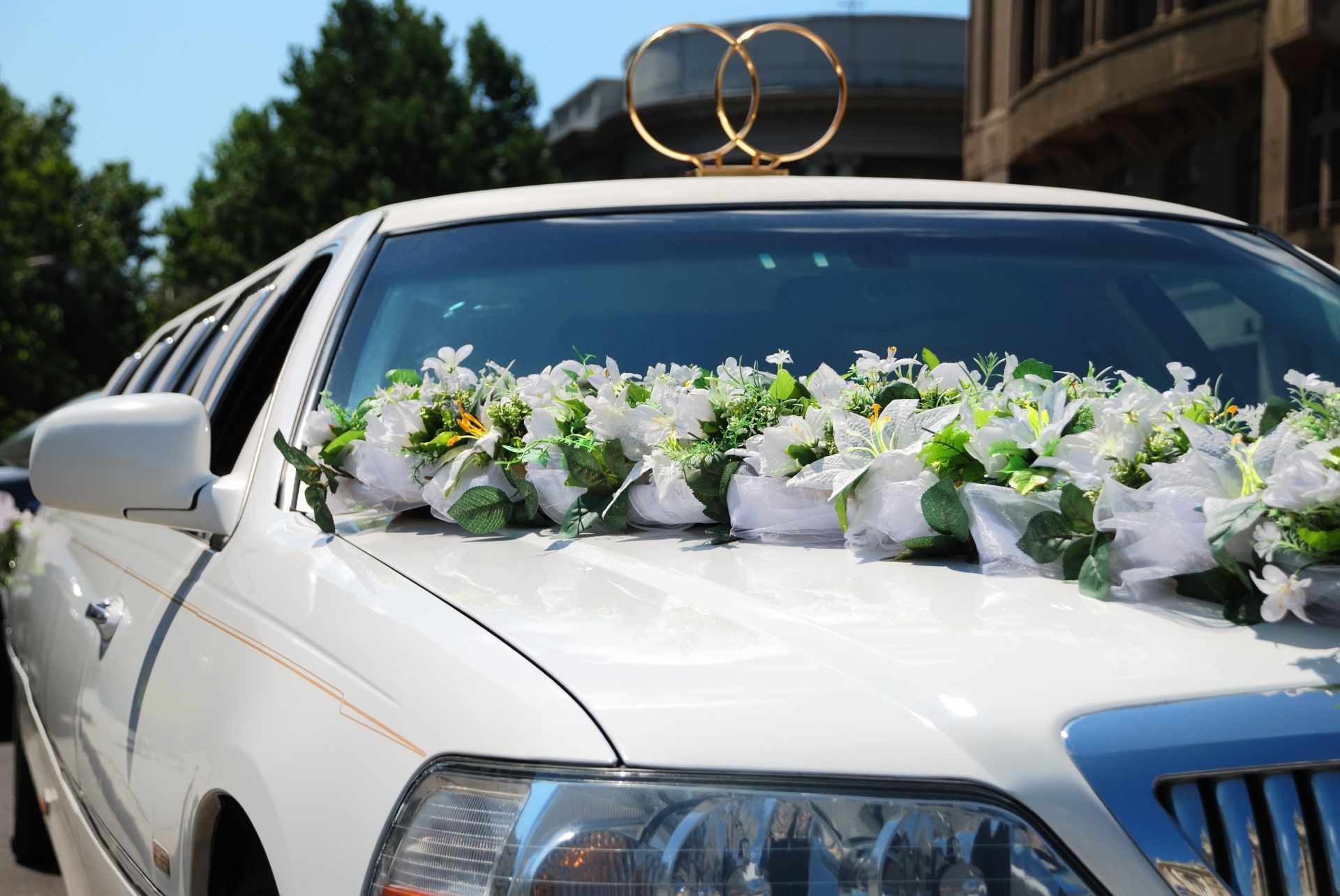 White limousine decorated with flowers and gold rings on the hood, ready for a wedding.