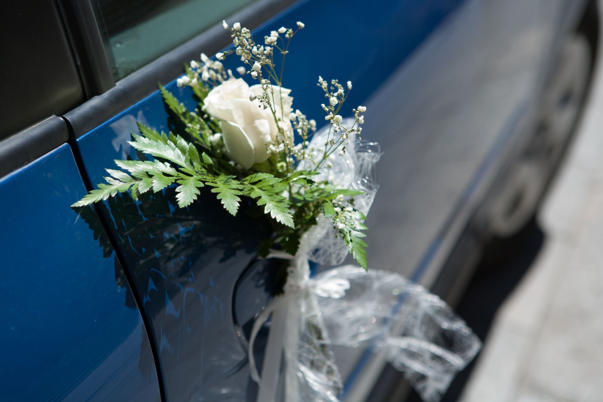 Blue car door decorated with white rose, greenery, and white ribbons.
